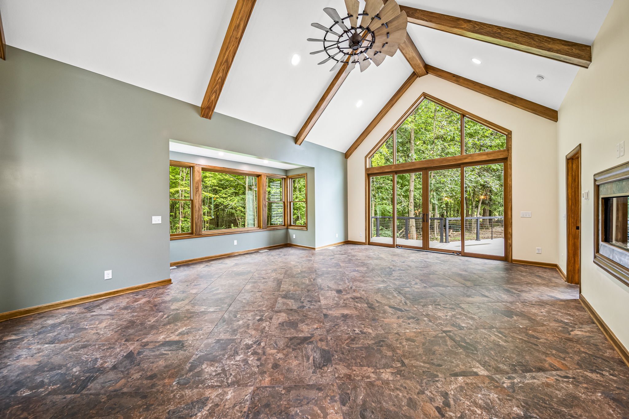 Vaulted great room with exposed timber beams, wall of windows overlooking forest, wide-plank floors, and open-concept layout — custom estate by Skoda Construction, Northeast Ohio