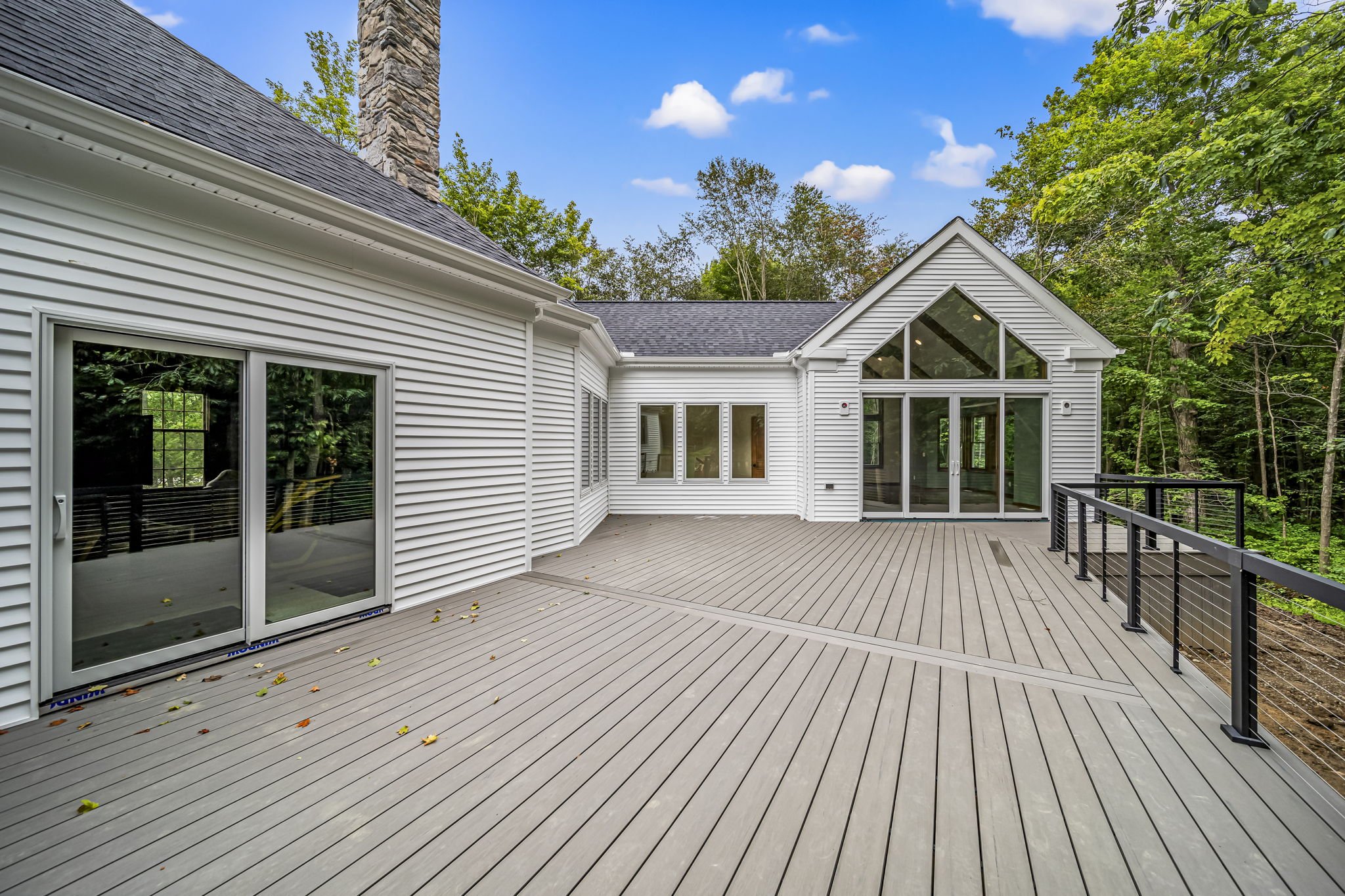 Expansive composite deck with cable railing overlooking wooded lot, large picture windows and stone chimney — custom home outdoor living by Skoda Construction, Northeast Ohio