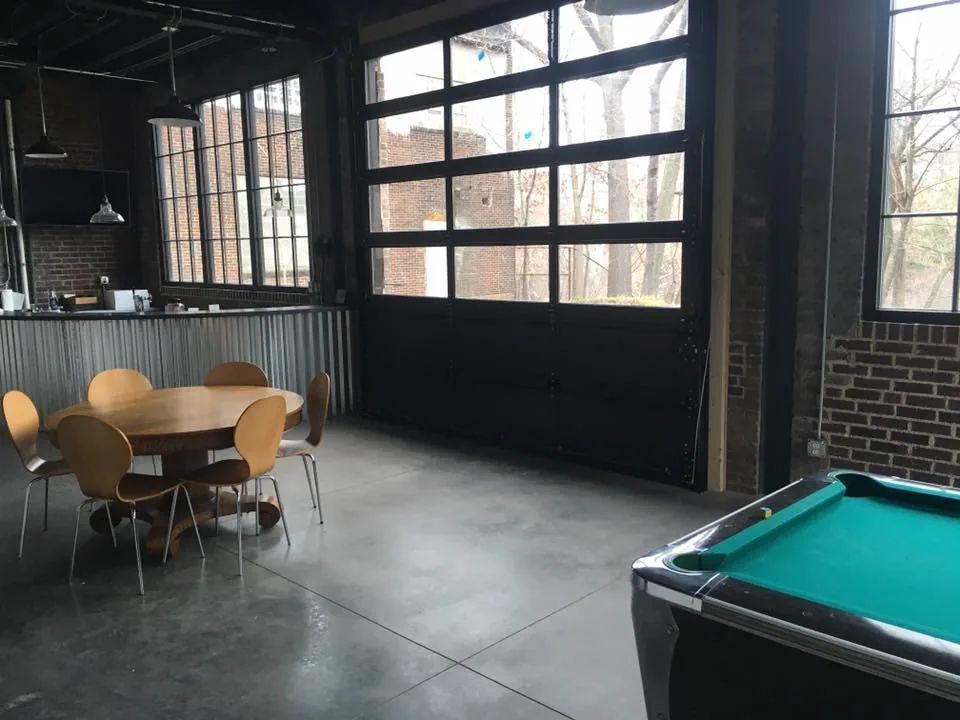 Industrial game room with pool table, steel-frame garage doors, brick walls, and polished concrete floor — commercial venue build-out by Skoda Construction, Northeast Ohio