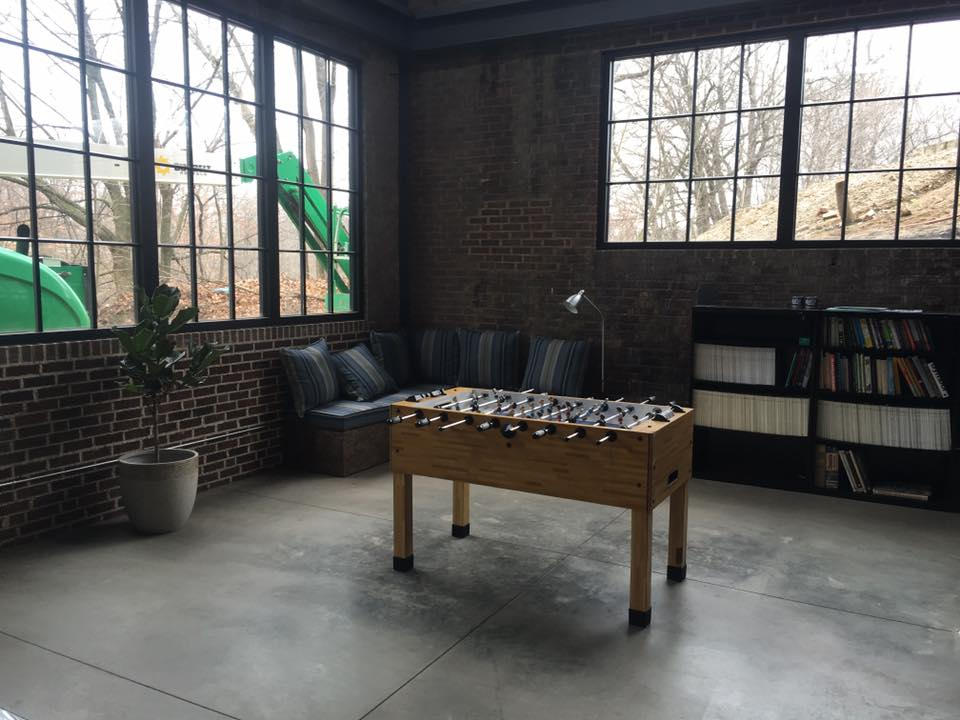 Industrial lounge with foosball table, exposed brick walls, steel factory windows, and polished concrete — commercial renovation by Skoda Construction, Northeast Ohio