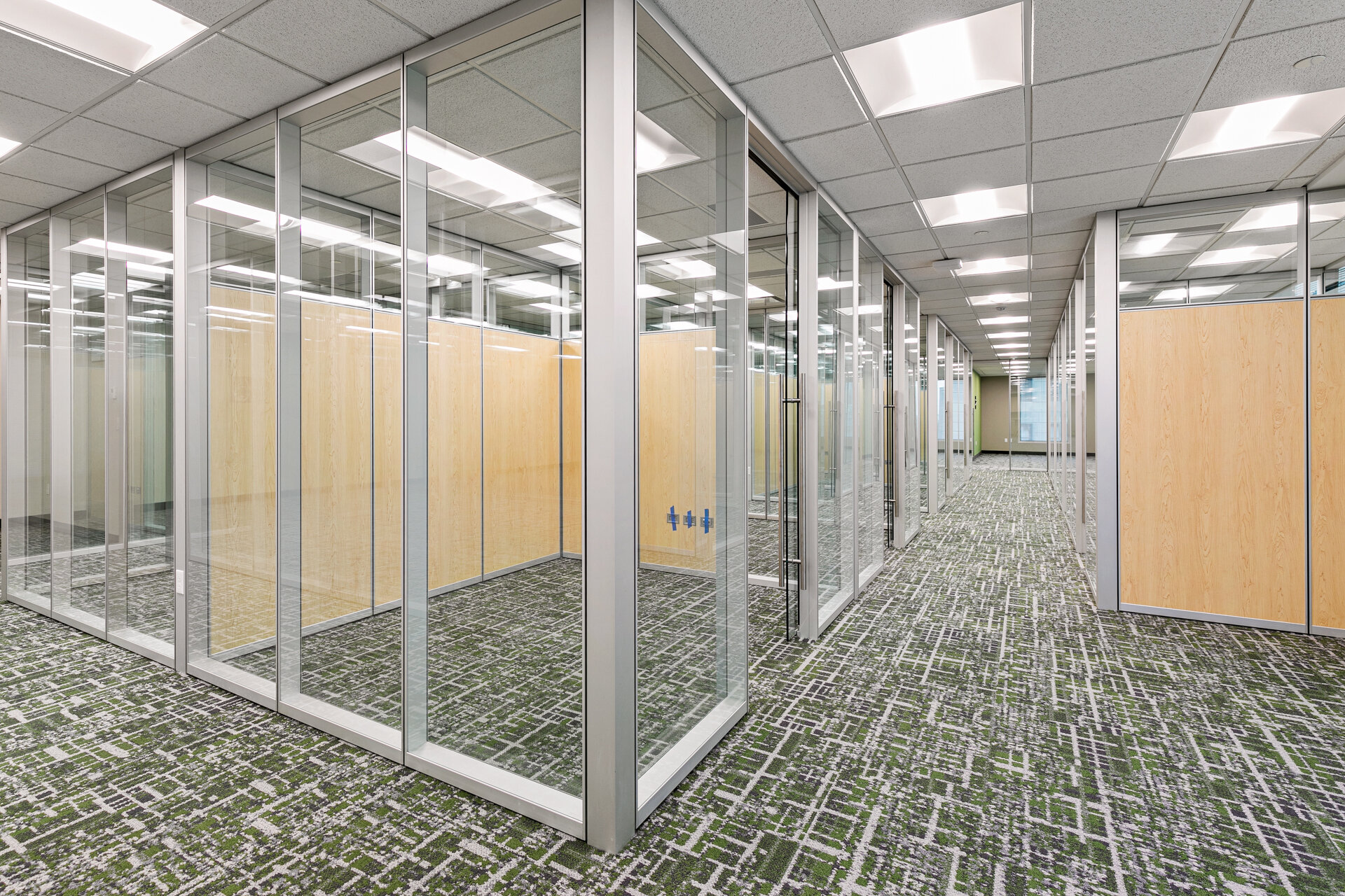 Symmetrical glass-walled hallway with private offices and wood accent panels — commercial tenant improvement by Skoda Construction, Northeast Ohio