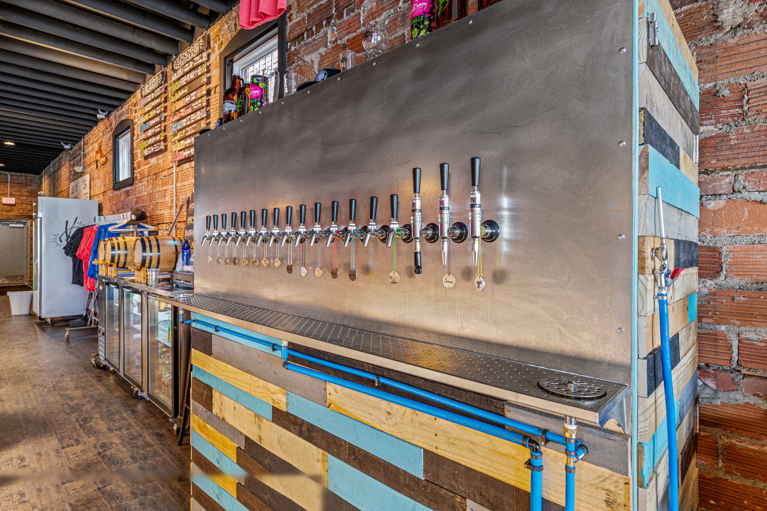 Stainless steel tap wall with 16 beer taps, reclaimed pallet wood bar front, and exposed brick walls — VooDoo Brewery by Skoda Construction
