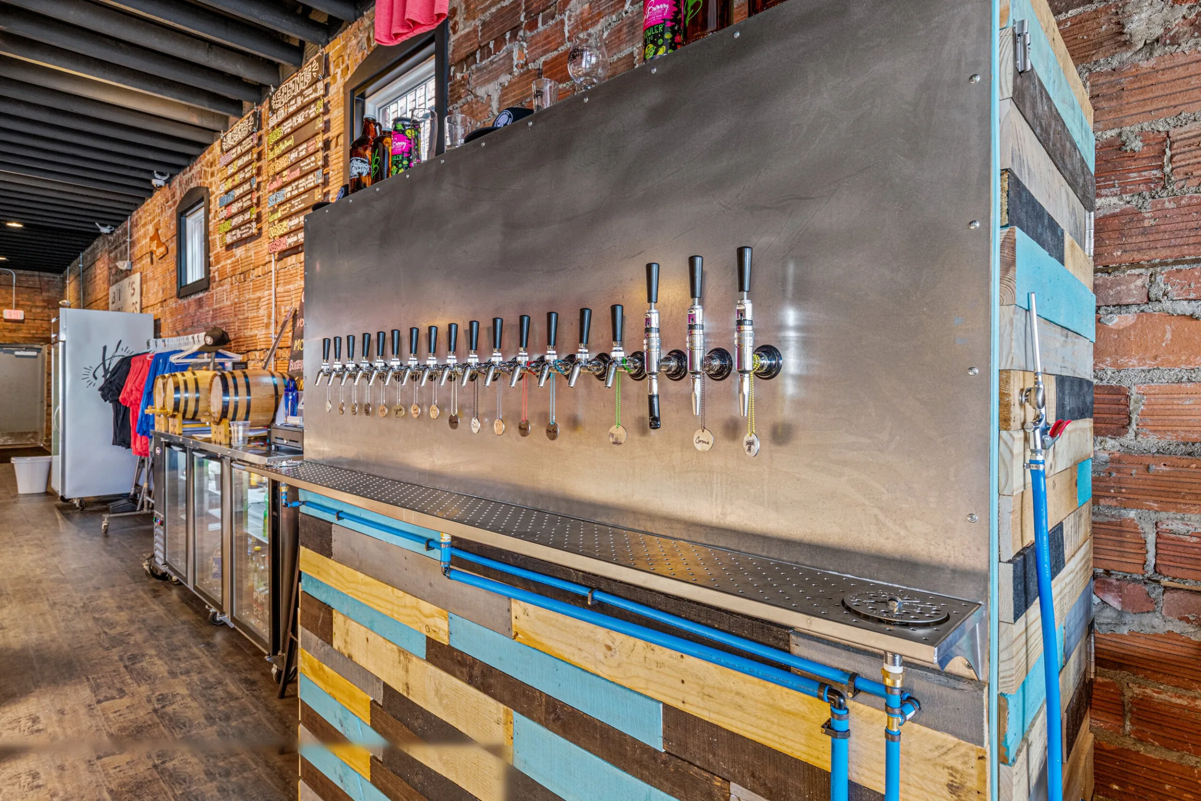 Stainless steel tap wall with 16 beer taps, reclaimed pallet wood bar front, and exposed brick walls — VooDoo Brewery by Skoda Construction