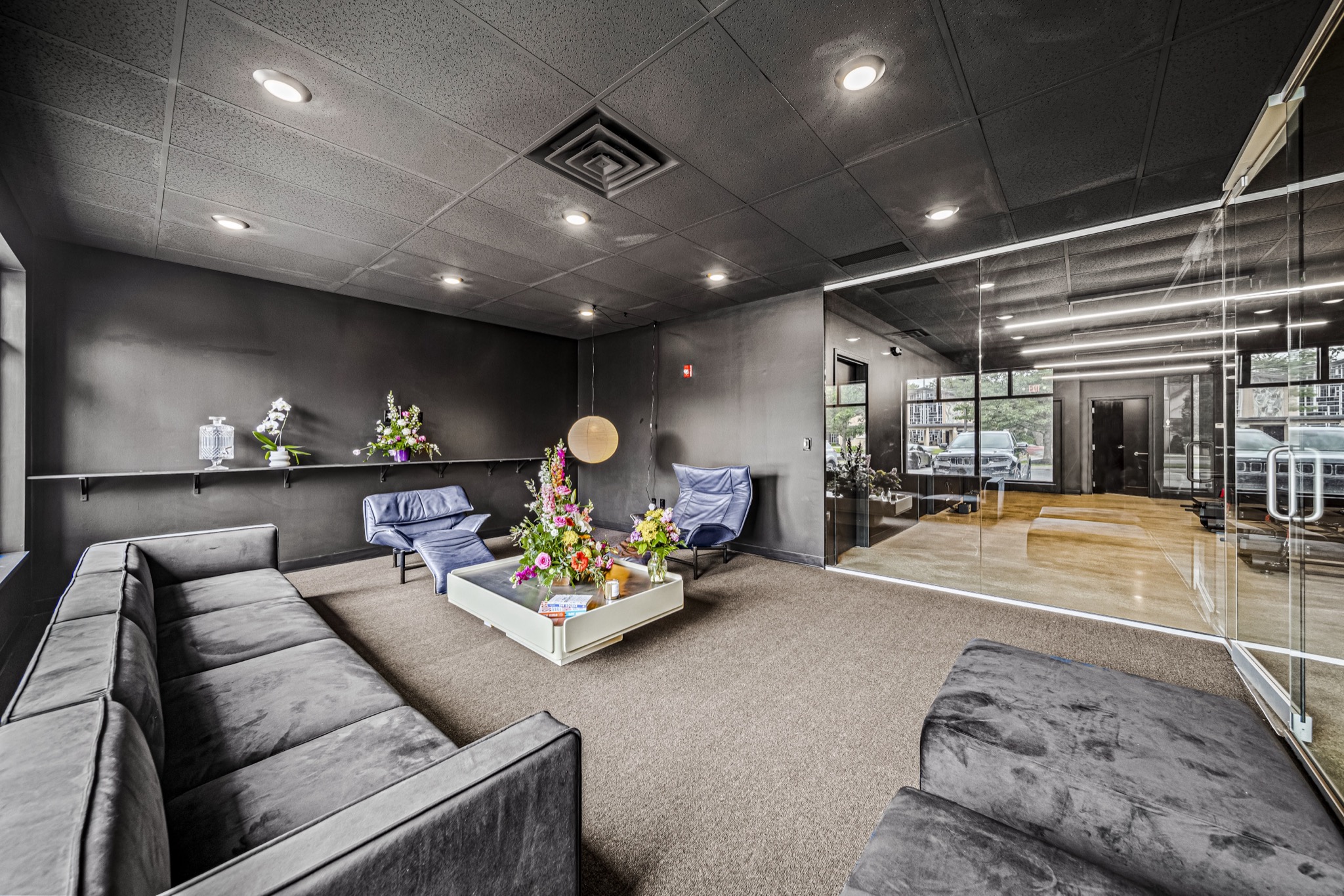Modern fitness studio lounge with dark walls, designer seating, and glass partition — commercial construction by Skoda Construction, Northeast Ohio