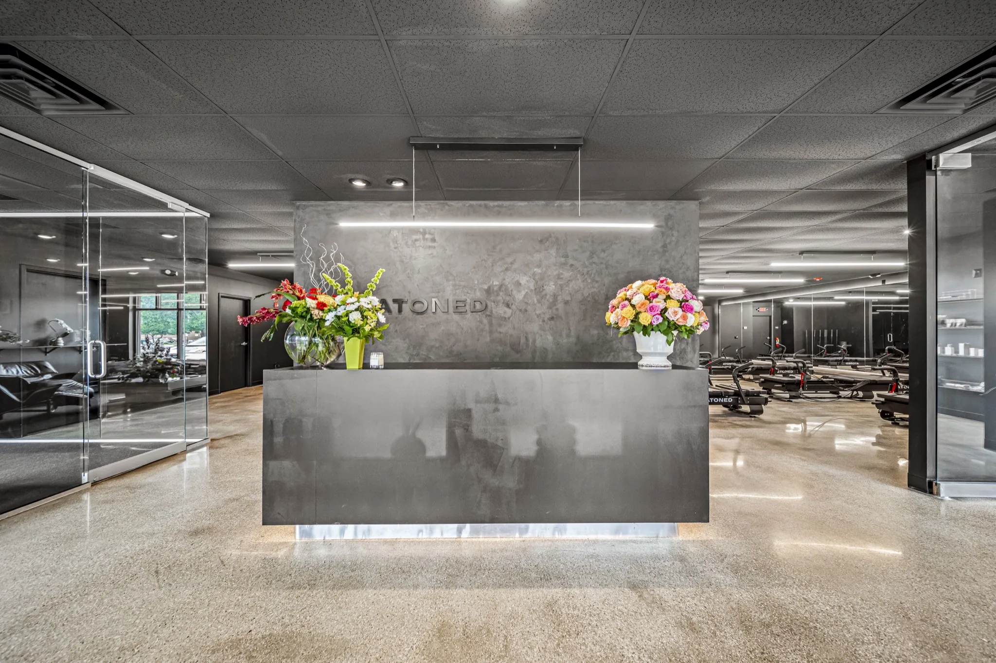 Premium fitness studio reception area with branded concrete feature wall, fresh flowers, and glass-walled studio views — commercial construction by Skoda Construction, Northeast Ohio