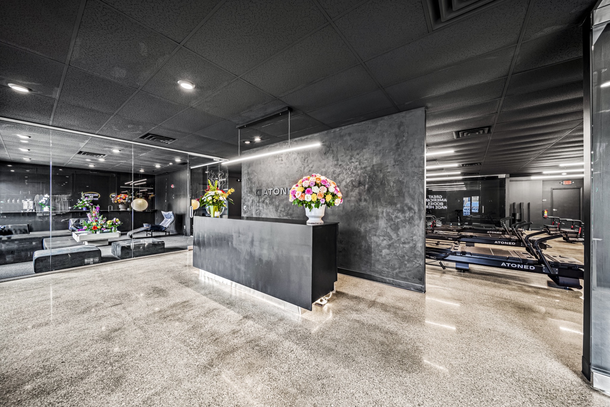 Wide-angle view of luxury fitness studio reception with polished concrete floors, dark ceiling, and full studio visibility — commercial design-build by Skoda Construction, Northeast Ohio