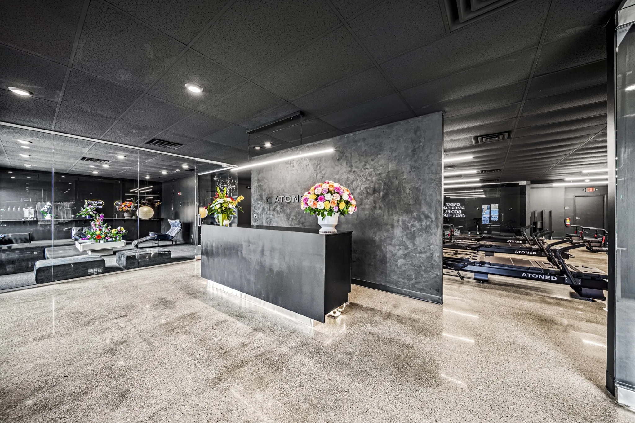 Wide-angle view of luxury fitness studio reception with polished concrete floors, dark ceiling, and full studio visibility — commercial design-build by Skoda Construction, Northeast Ohio
