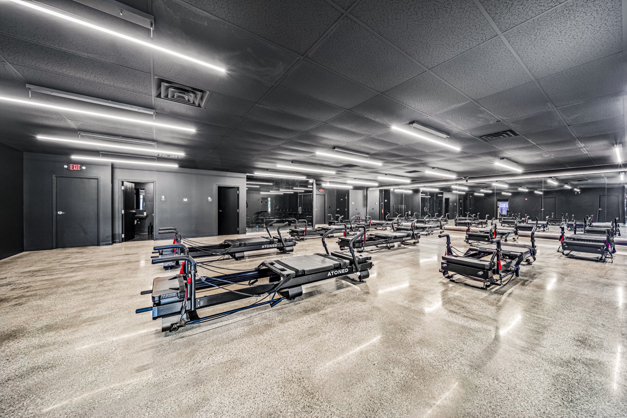 Pilates reformer studio with linear LED lighting, polished concrete floors, and dark industrial ceiling — commercial fitness build-out by Skoda Construction, Northeast Ohio
