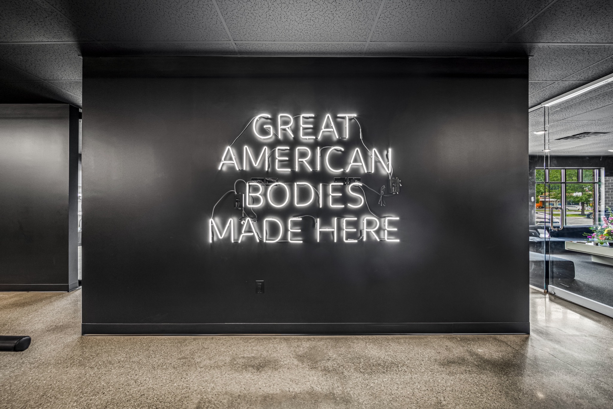 Custom neon wall sign reading Great American Bodies Made Here against matte dark wall — detail work by Skoda Construction, Northeast Ohio