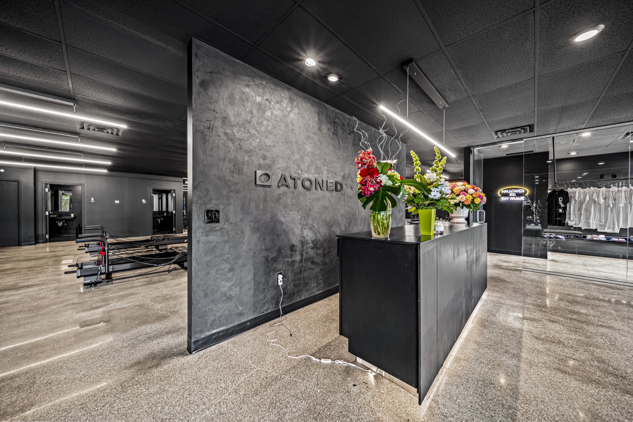 Fitness studio branded reception wall with floral arrangements and glass-walled studio beyond — commercial build-out by Skoda Construction, Northeast Ohio