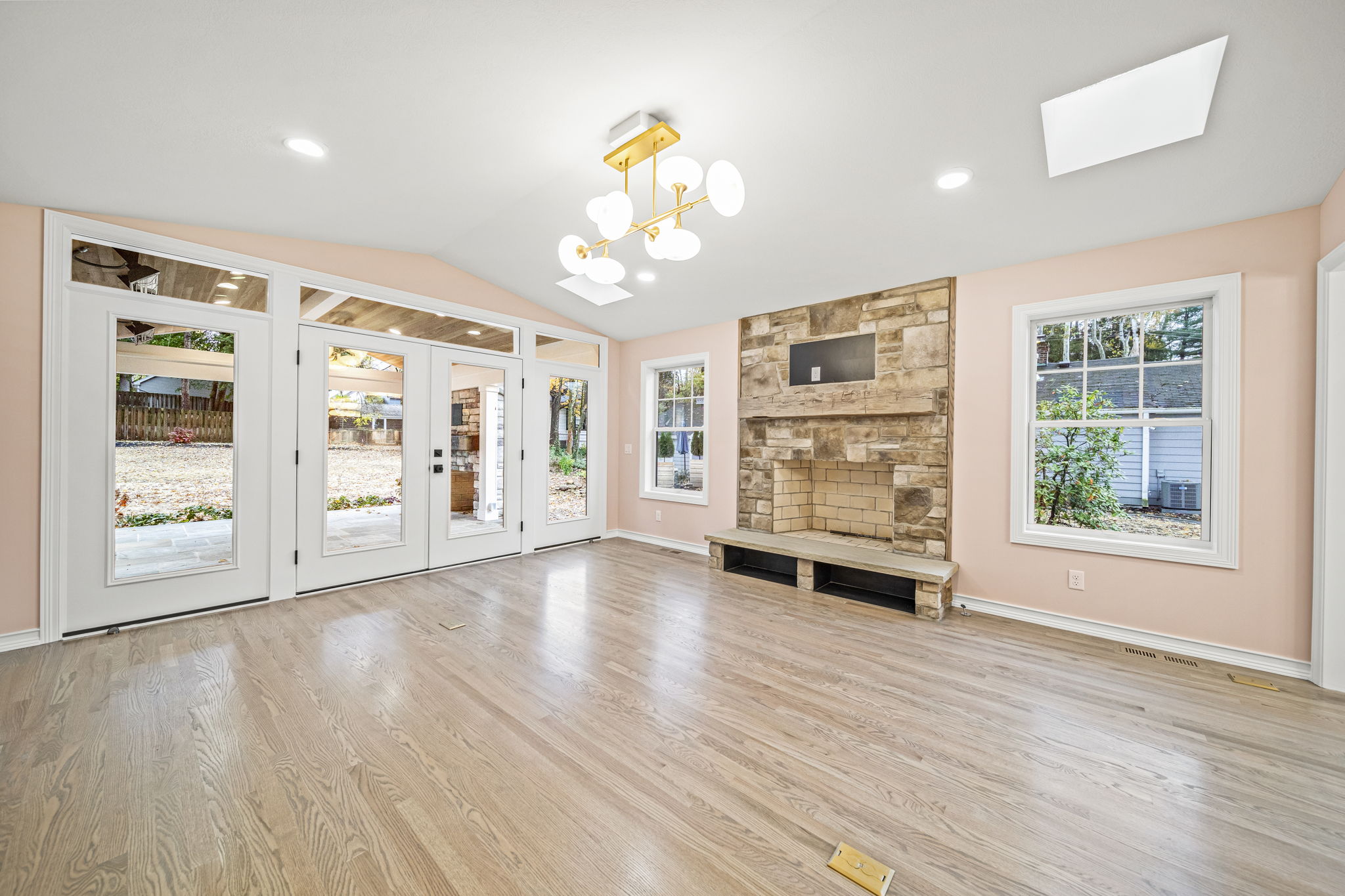 Open-concept living room with natural stone fireplace, french doors to patio, and brass chandelier — custom farmhouse by Skoda Construction, Northeast Ohio
