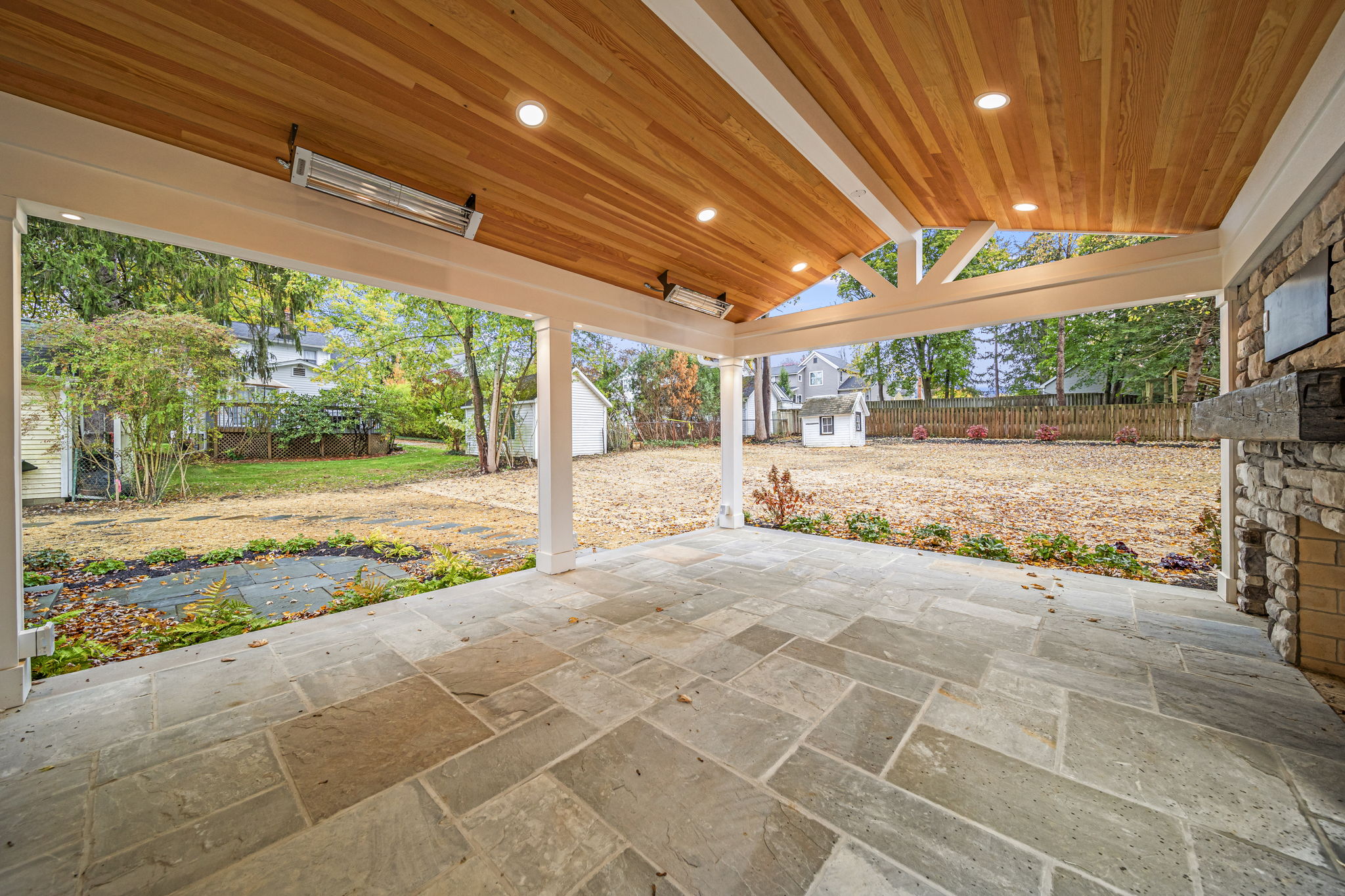 Covered patio with cedar plank ceiling, natural stone flooring, and outdoor fireplace — luxury outdoor living by Skoda Construction, Northeast Ohio