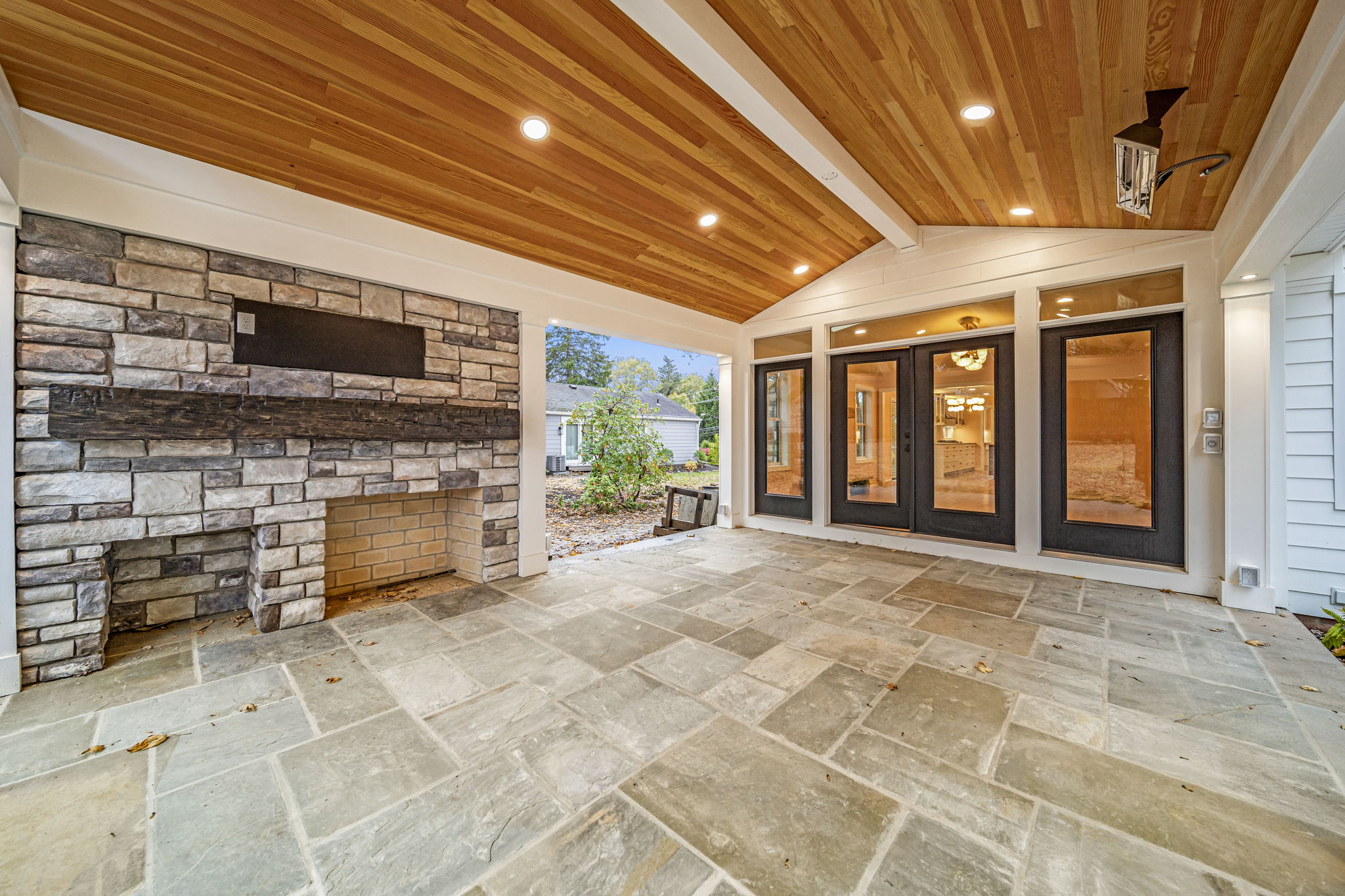 Outdoor stone fireplace with TV mount under cedar-clad covered patio — custom home by Skoda Construction, Northeast Ohio