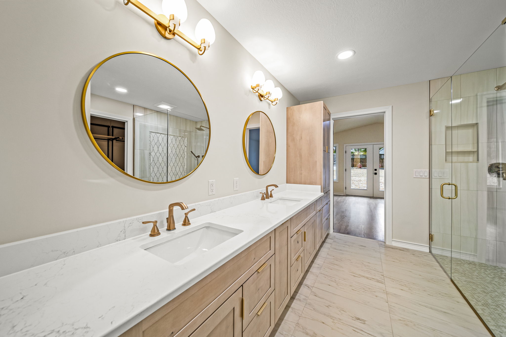 Luxurious primary bathroom with double vanity, gold-framed mirrors, brass fixtures, and frameless glass shower — custom home by Skoda Construction, Northeast Ohio