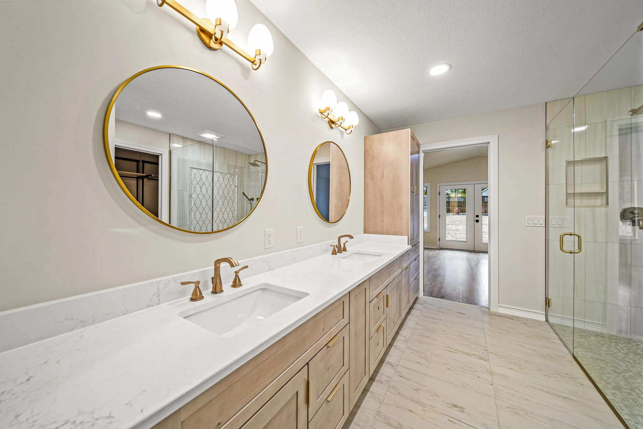 Luxurious primary bathroom with double vanity, gold-framed mirrors, brass fixtures, and frameless glass shower — custom home by Skoda Construction, Northeast Ohio
