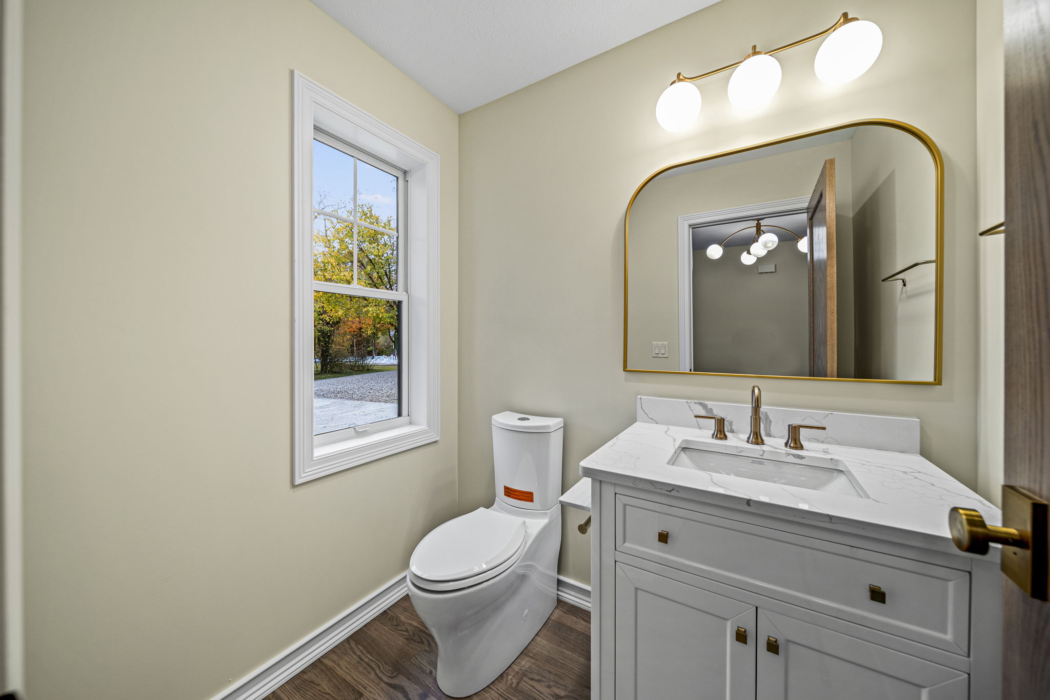 Elegant powder room with gold-framed arched mirror, brass vanity light, white marble countertop, and grey shaker vanity — modern farmhouse by Skoda Construction, Northeast Ohio