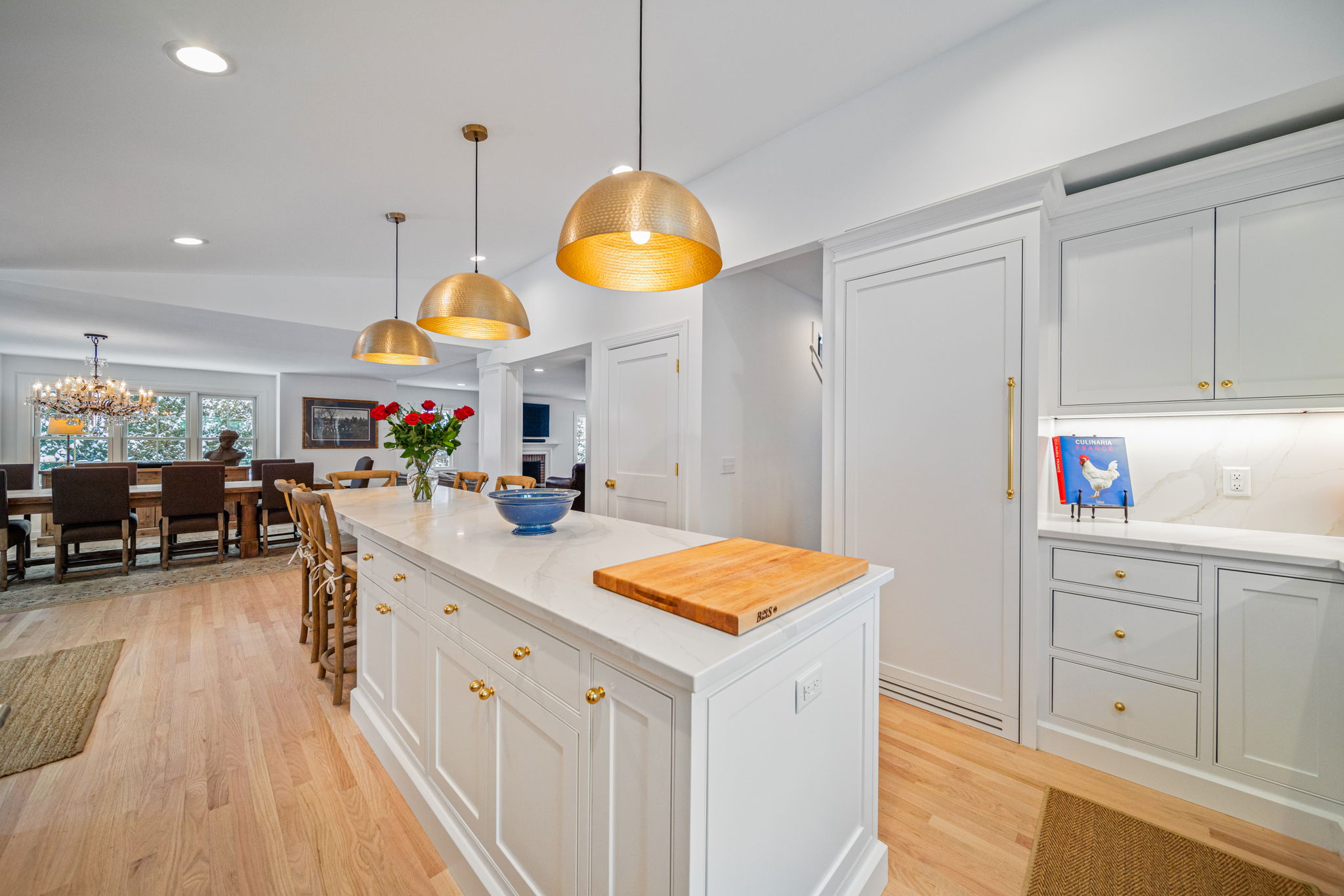 White kitchen island with brass hardware and three gold pendant lights over marble countertops — luxury kitchen renovation by Skoda Construction, Northeast Ohio