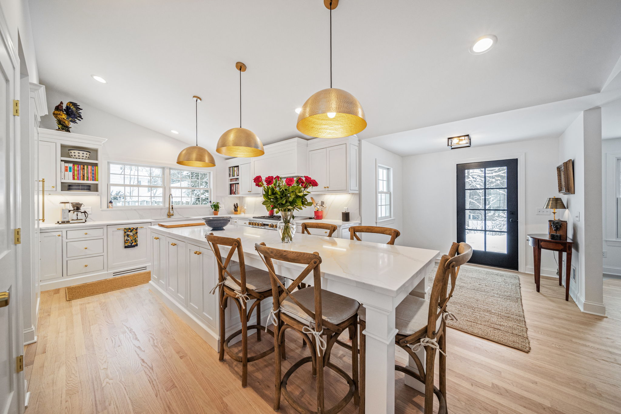 Bright white kitchen with gold pendant trio, island seating, and black glass entry door — whole-home renovation by Skoda Construction, Northeast Ohio