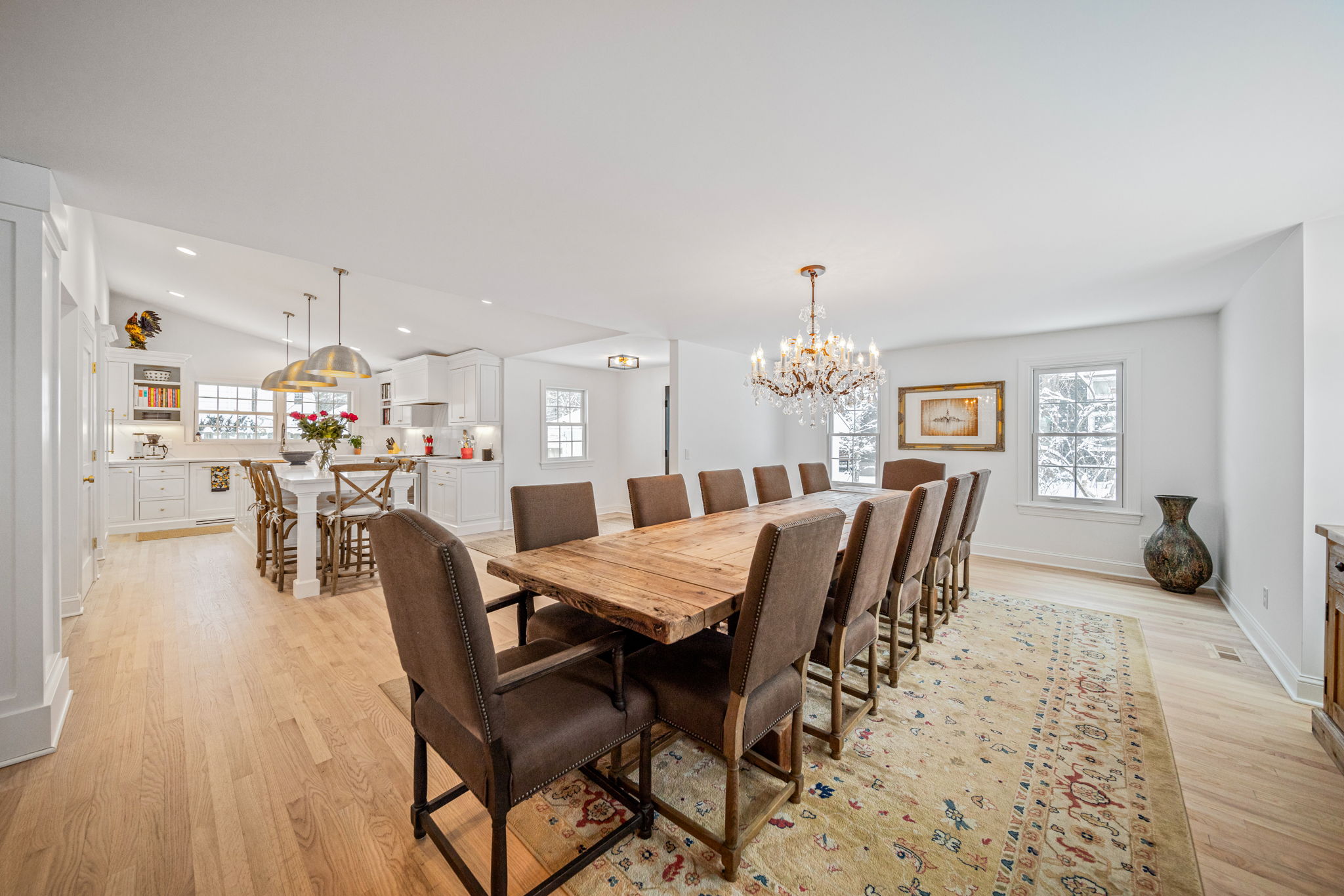 Grand dining room with crystal chandelier, twelve-seat wood table, and open kitchen beyond — luxury home renovation by Skoda Construction, Northeast Ohio