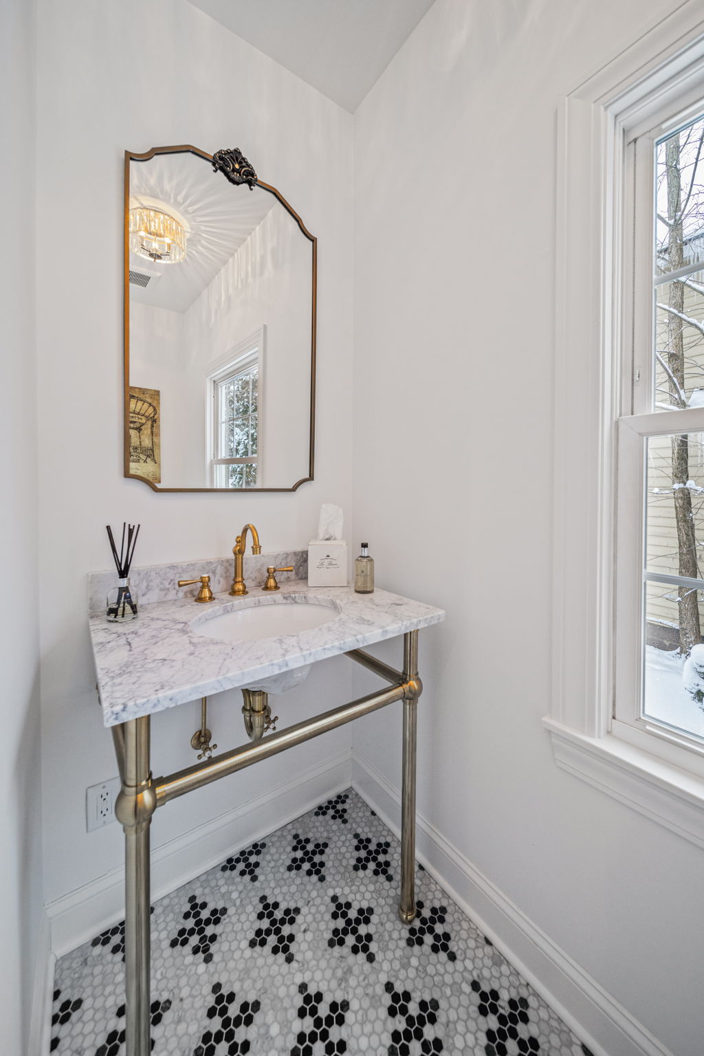 Elegant powder room with marble console sink, brass faucet, vintage mirror, and black-and-white hex tile floor — bathroom renovation by Skoda Construction, Northeast Ohio