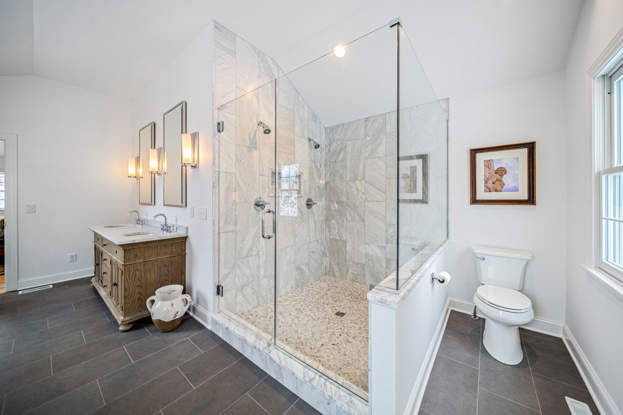Custom marble walk-in shower with glass enclosure, pebble floor, and wood vanity — master bath renovation by Skoda Construction, Northeast Ohio