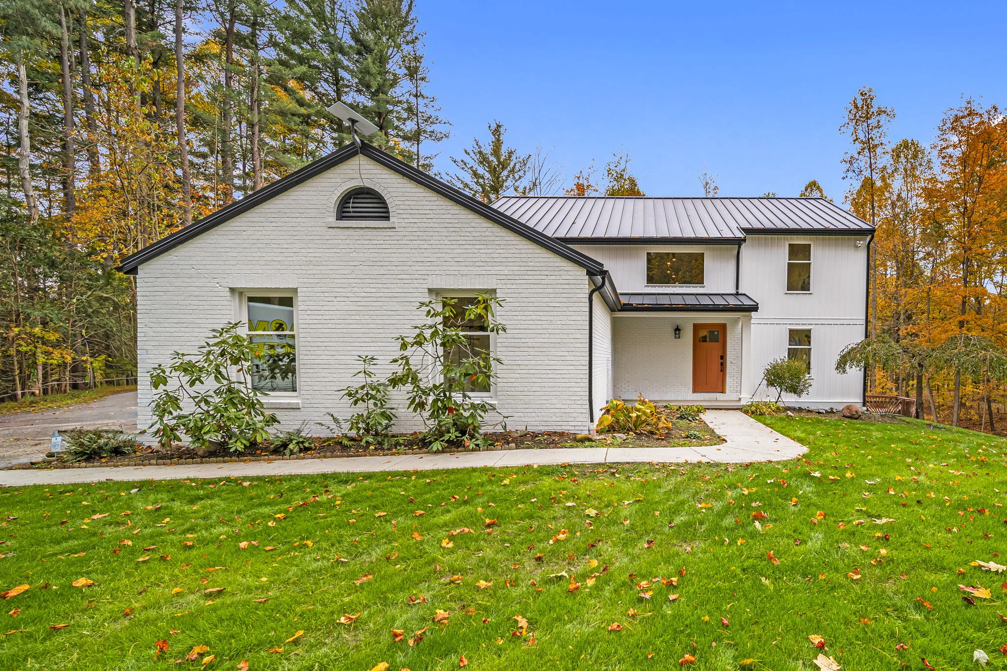 Modern white brick and board-and-batten home with metal roof surrounded by fall foliage — custom residential by Skoda Construction, Northeast Ohio