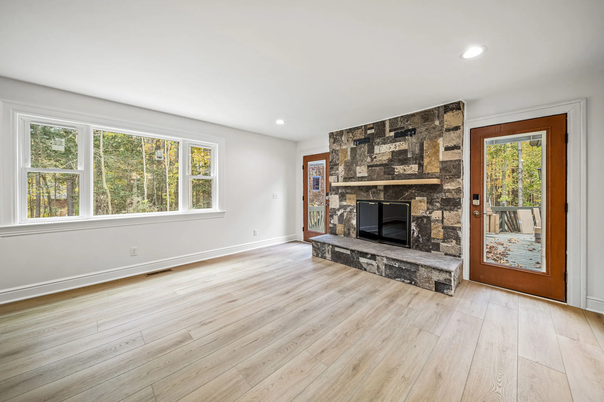 Living room with floor-to-ceiling natural stone fireplace and autumn woodland views — custom home by Skoda Construction, Northeast Ohio