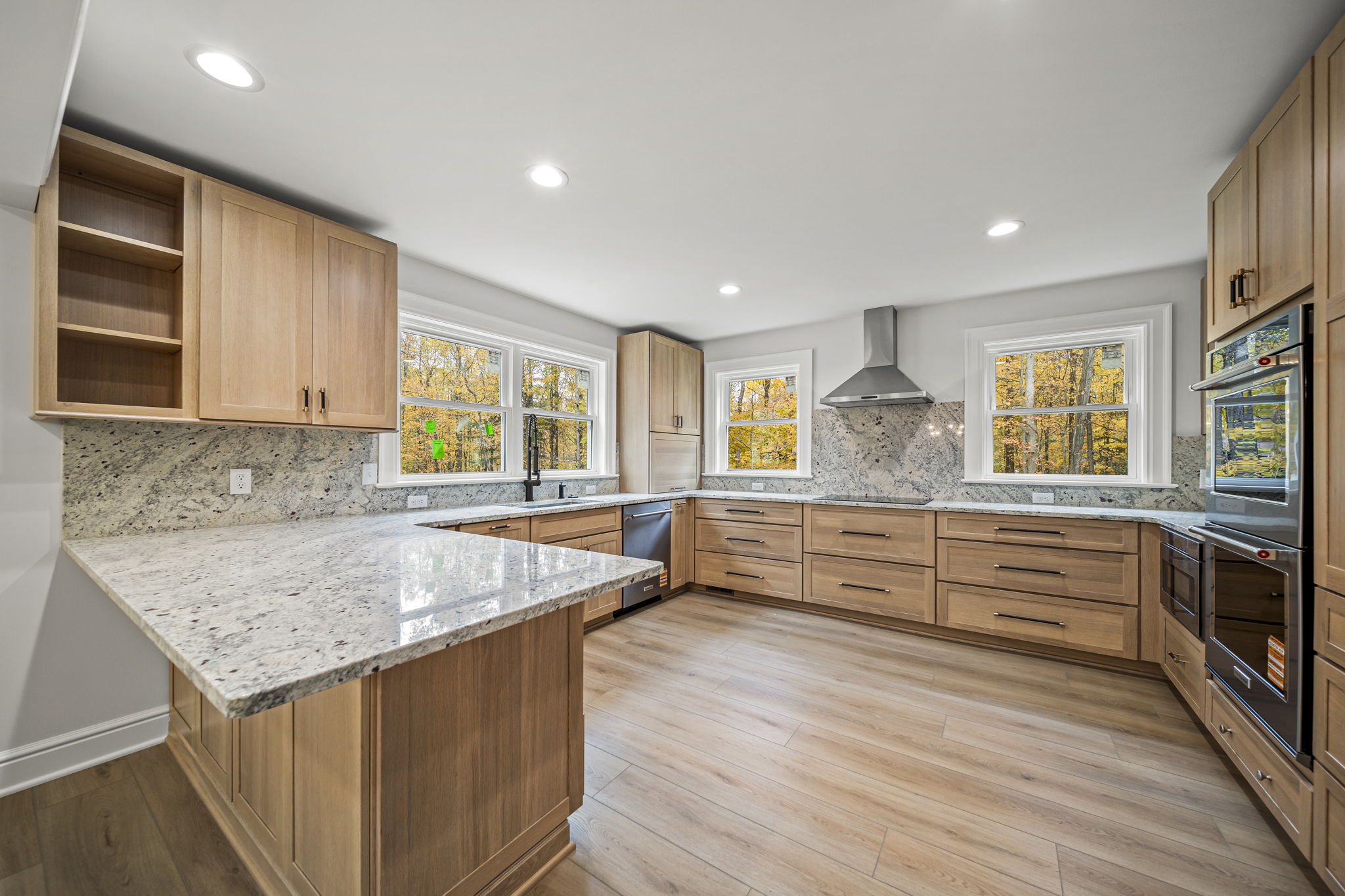 Natural white oak kitchen with granite countertops and wooded views through picture windows — custom home by Skoda Construction, Northeast Ohio