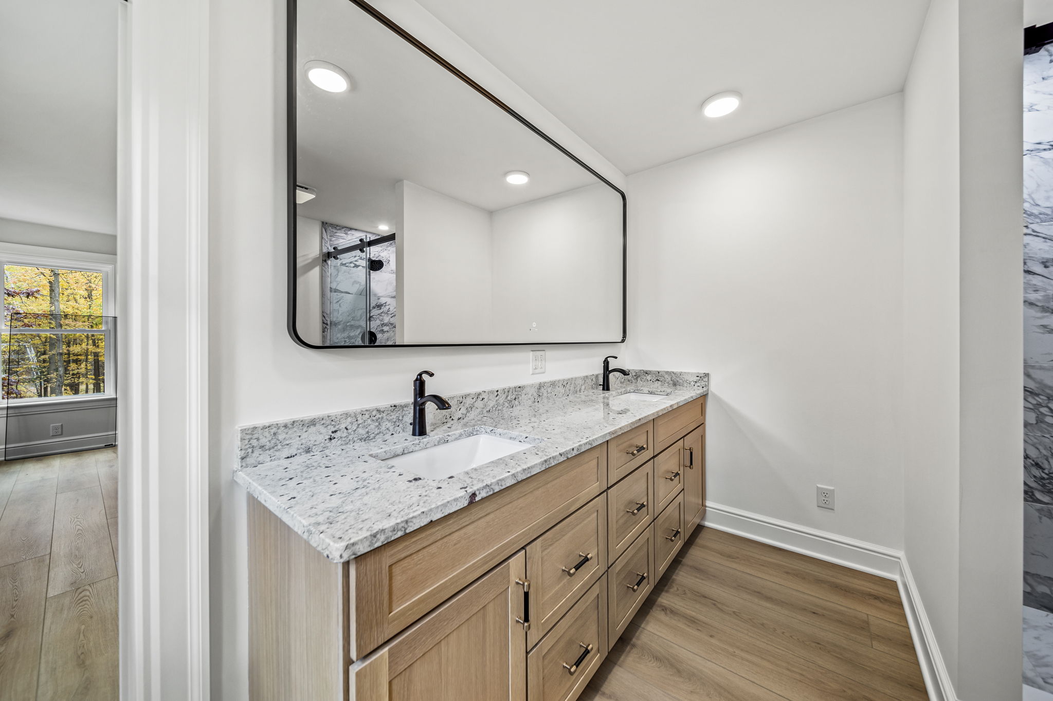 Primary bathroom double vanity with natural oak cabinetry, granite counter, and marble-look shower — luxury home by Skoda Construction, Northeast Ohio