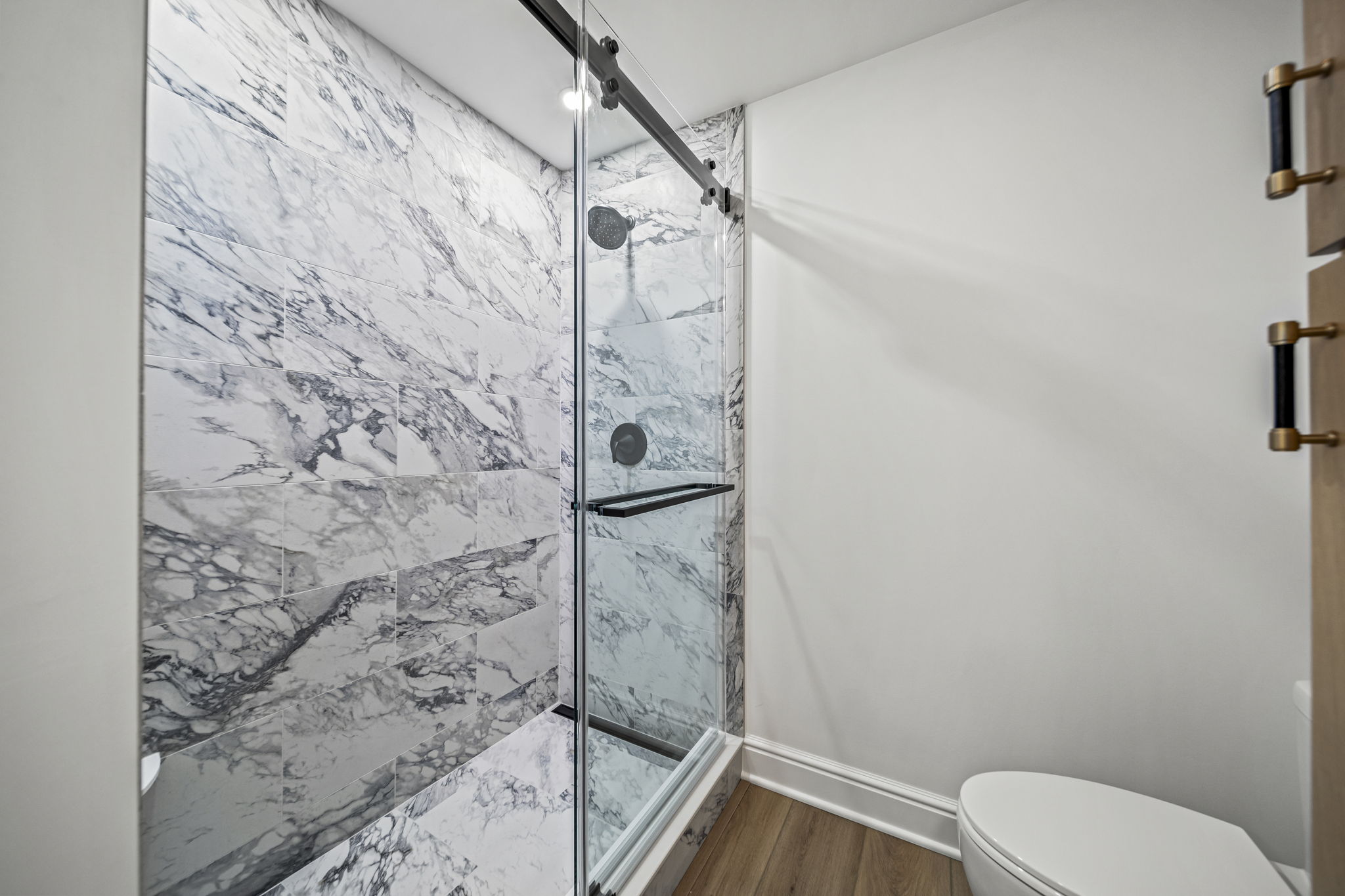 Dramatic marble-veined porcelain walk-in shower with barn-door glass enclosure and matte black hardware — custom bathroom by Skoda Construction, Northeast Ohio