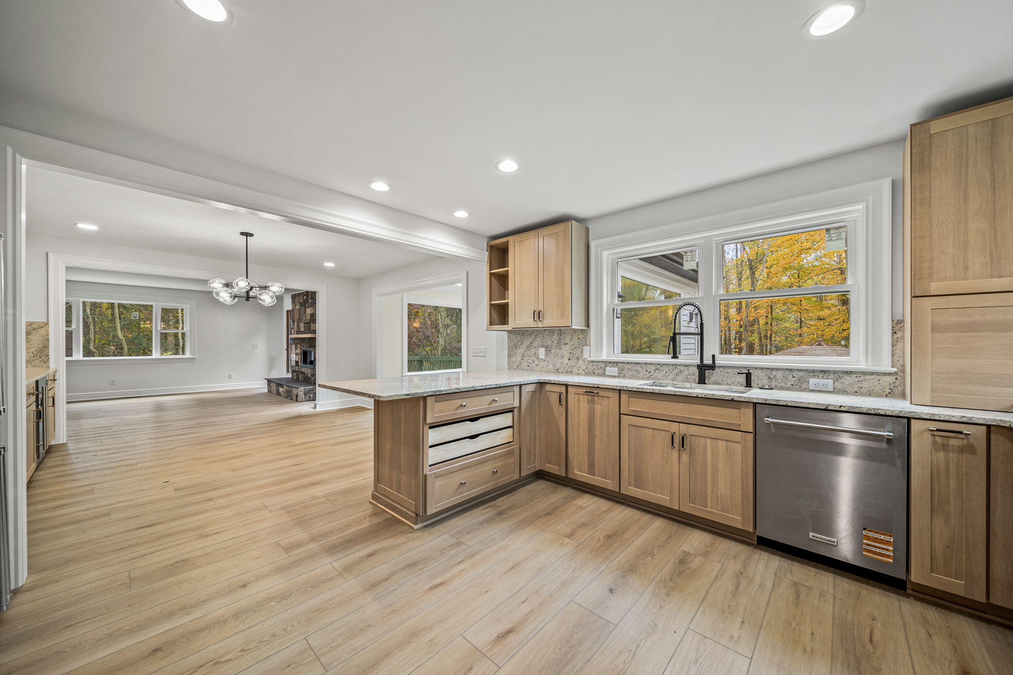 Open-concept kitchen with natural oak cabinets, granite backsplash, and sputnik chandelier opening to dining area — Skoda Construction custom home