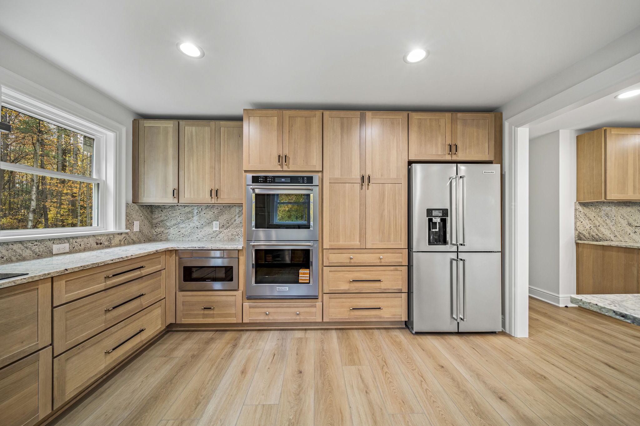 Kitchen appliance wall with natural white oak cabinetry, double wall ovens, microwave drawer, stainless fridge, and granite countertops — custom home by Skoda Construction, Northeast Ohio