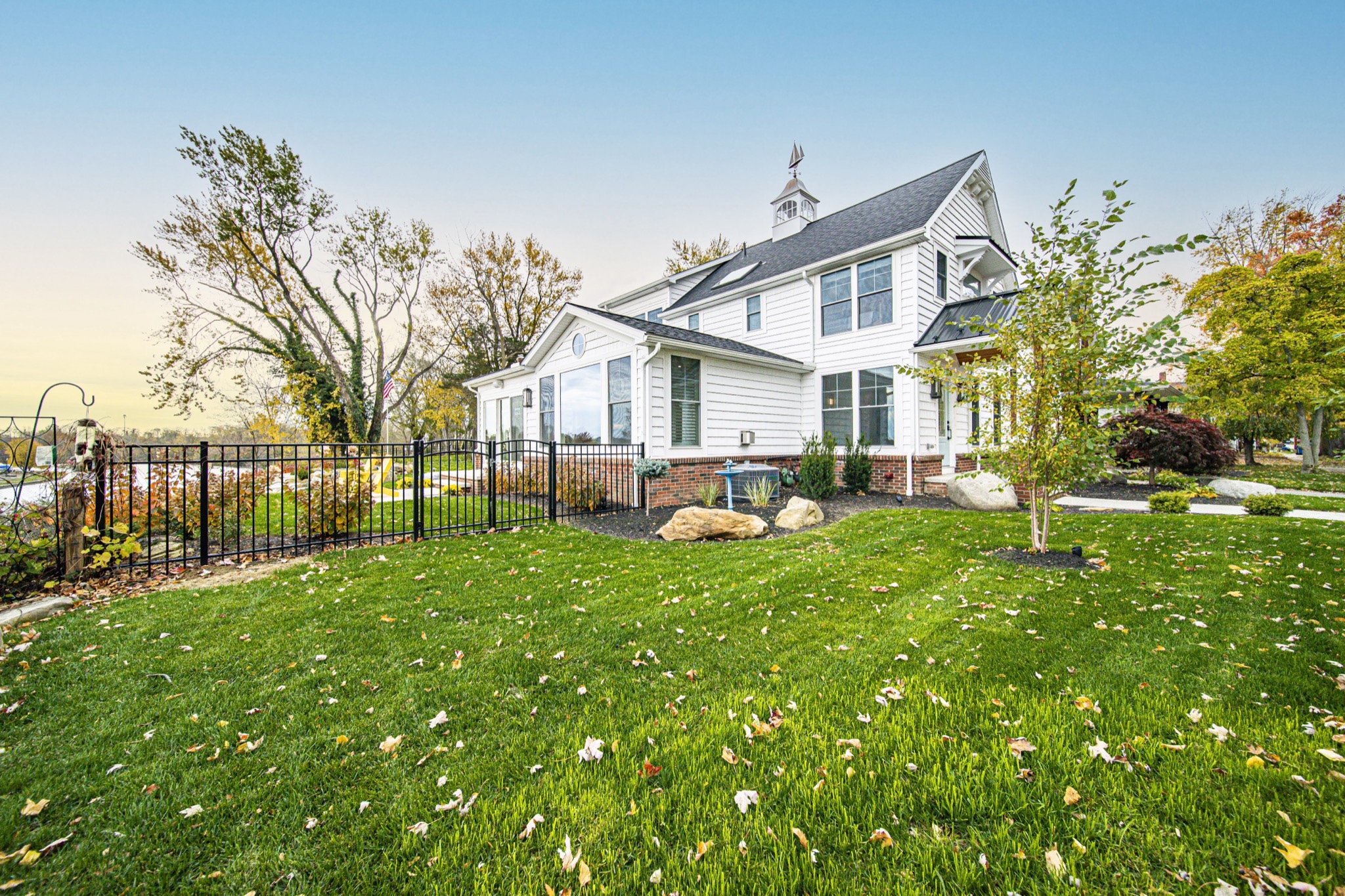White farmhouse rear view with cupola, iron fencing, and autumn foliage — custom residential build by Skoda Construction, Northeast Ohio