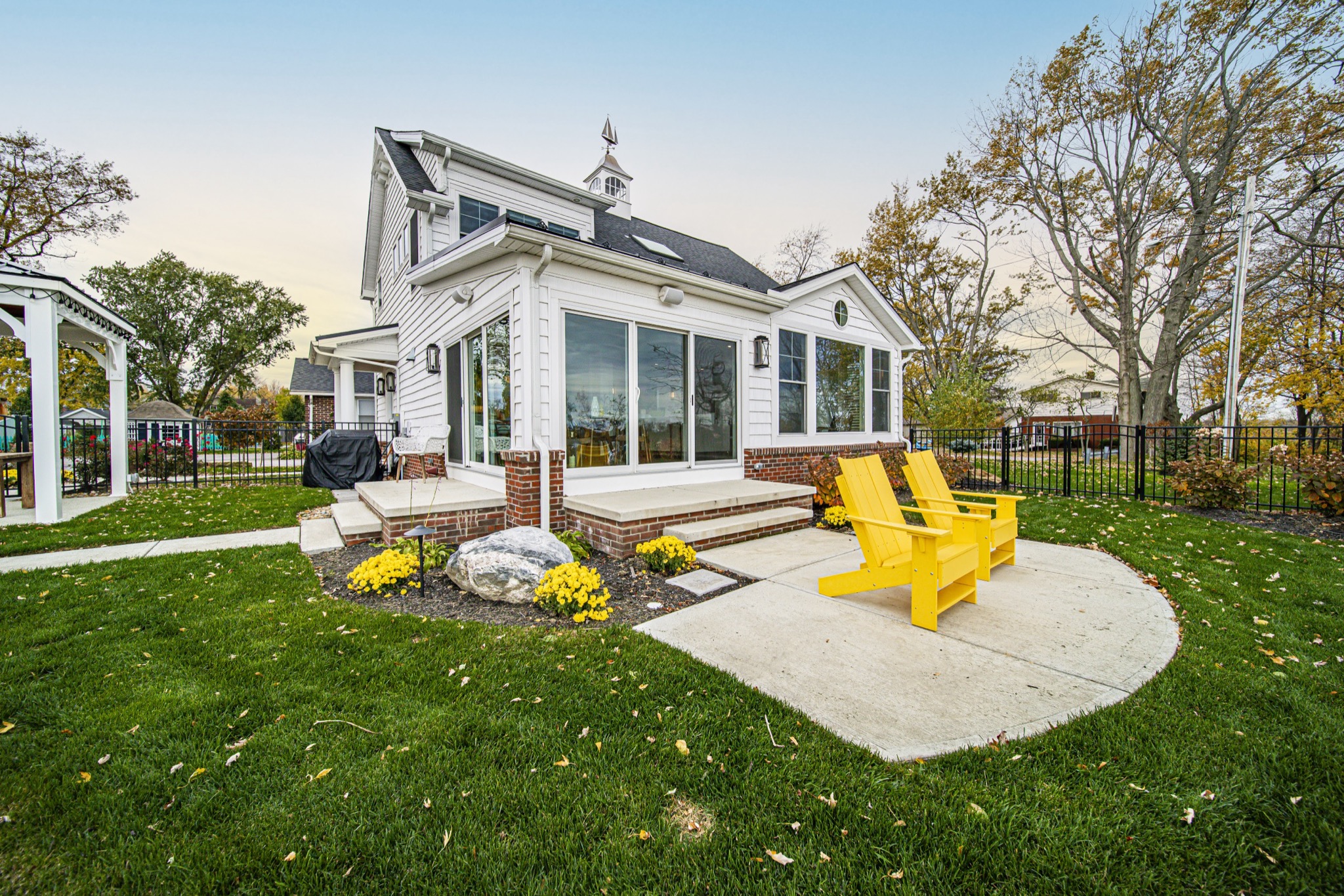 Custom patio with yellow Adirondack chairs and farmhouse sunroom with floor-to-ceiling windows — Skoda Construction, Northeast Ohio