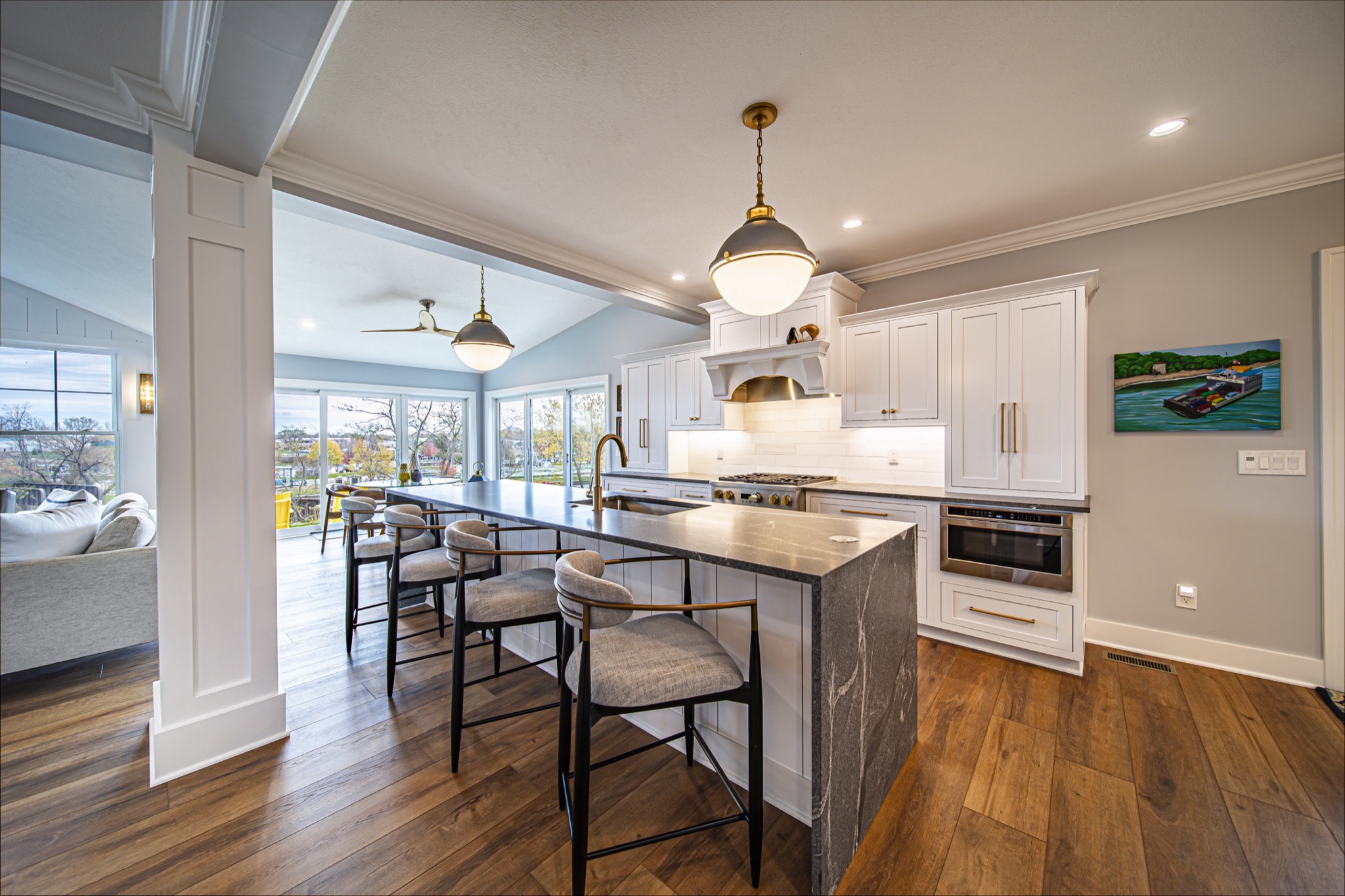 White kitchen with dark marble island, upholstered bar stools, and brass fixtures in open-concept farmhouse — Skoda Construction, Northeast Ohio