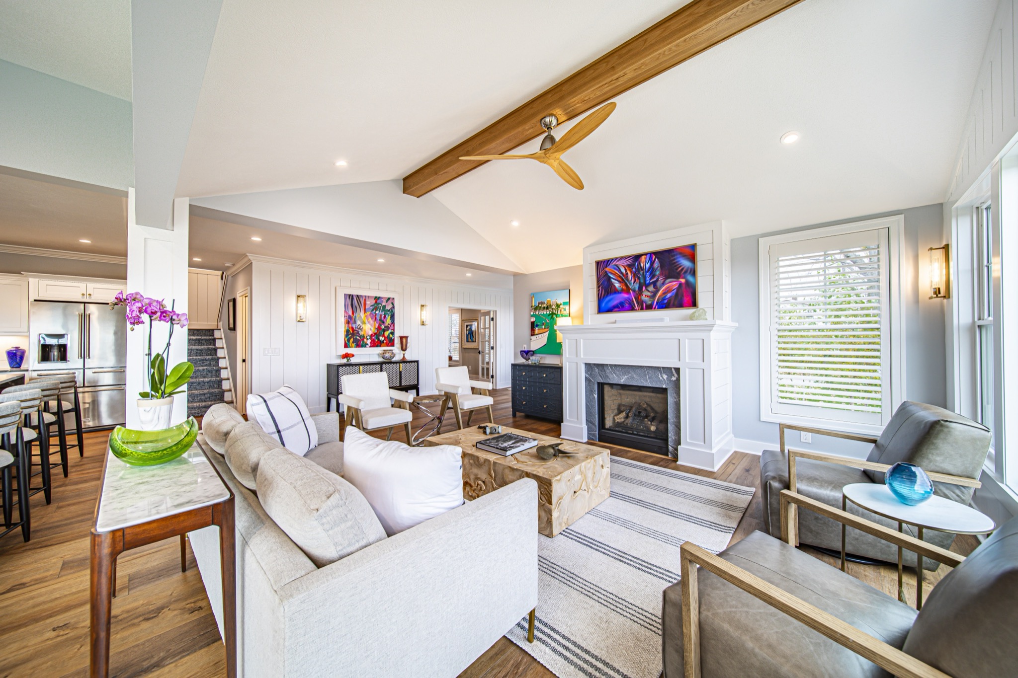 Open great room with exposed wood beam, shiplap fireplace wall, and brass sconces in farmhouse — luxury living by Skoda Construction, Northeast Ohio