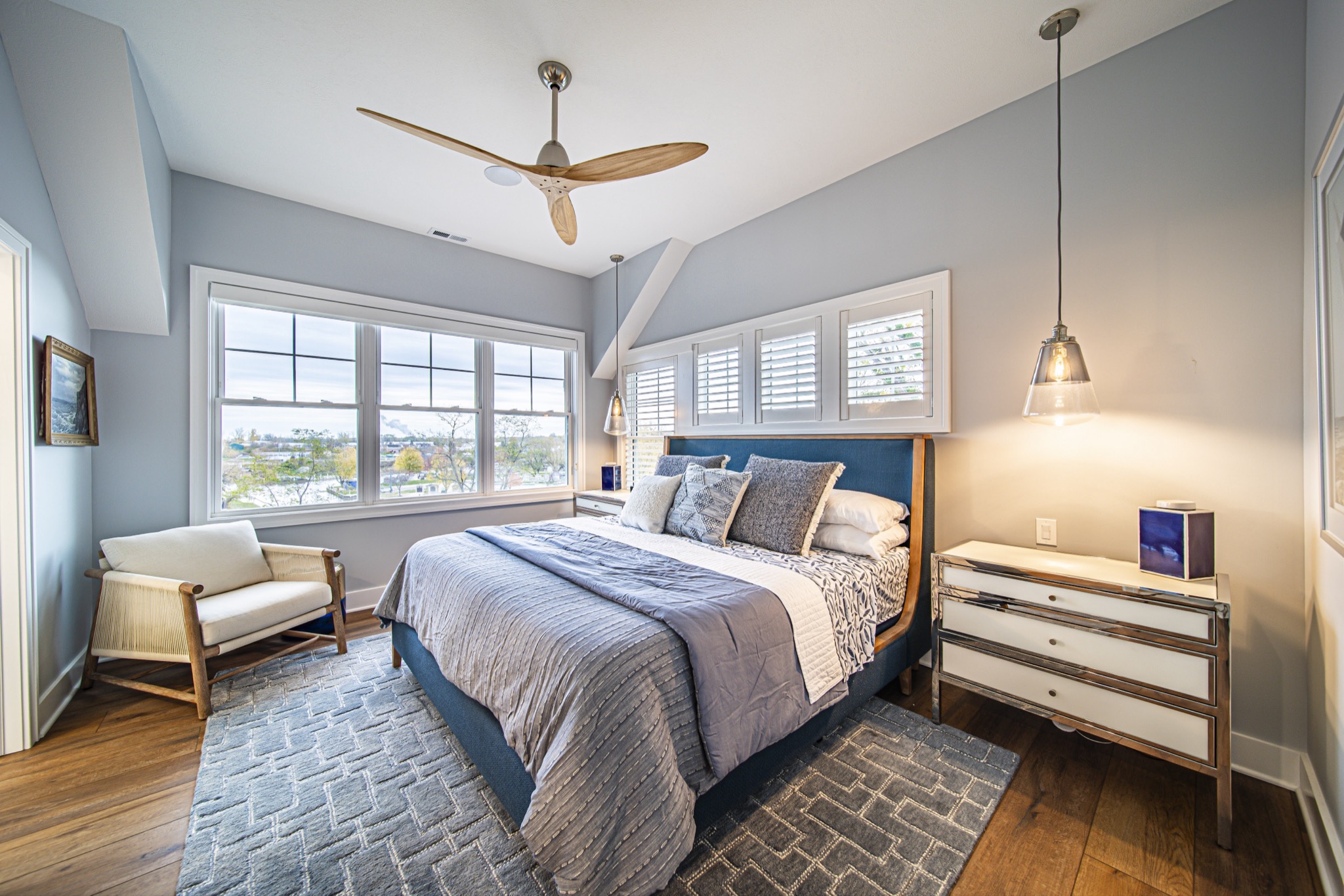 Master bedroom with vaulted ceiling, blue coastal palette, pendant light, and plantation shutters — custom home by Skoda Construction, Northeast Ohio