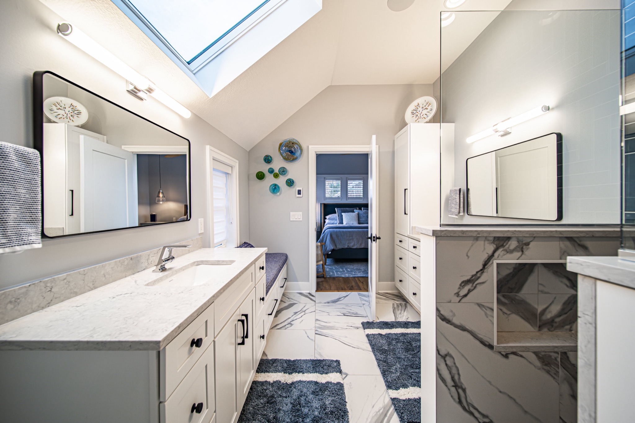 Primary bathroom with skylight, calacatta marble floor, glass shower enclosure, and dual vanities — custom bath by Skoda Construction, Northeast Ohio