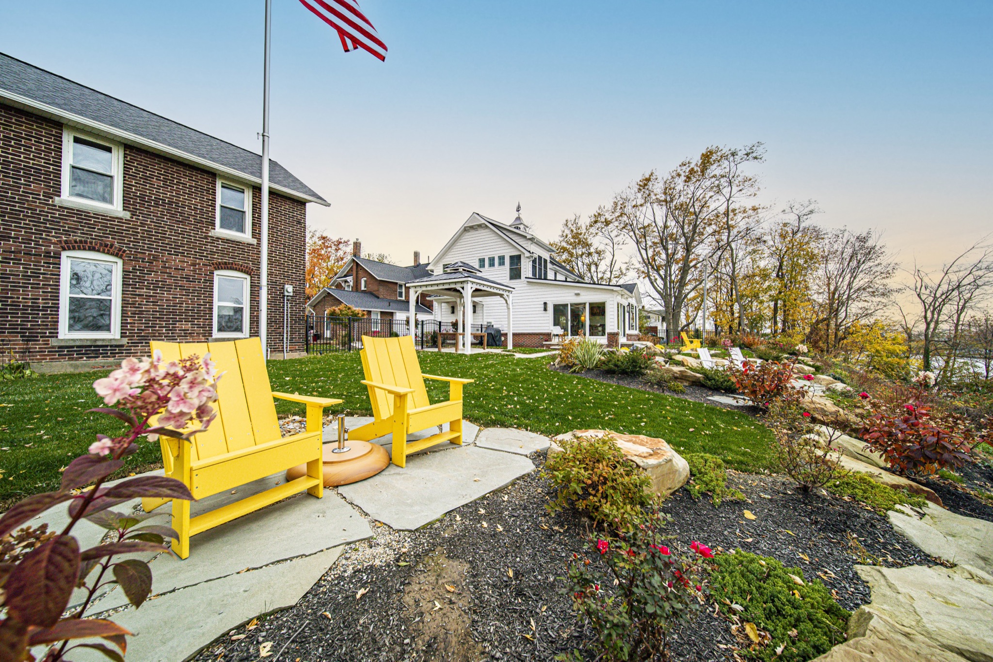Custom property overview with Adirondack seating, stone landscaping, and white farmhouse — Skoda Construction, Northeast Ohio
