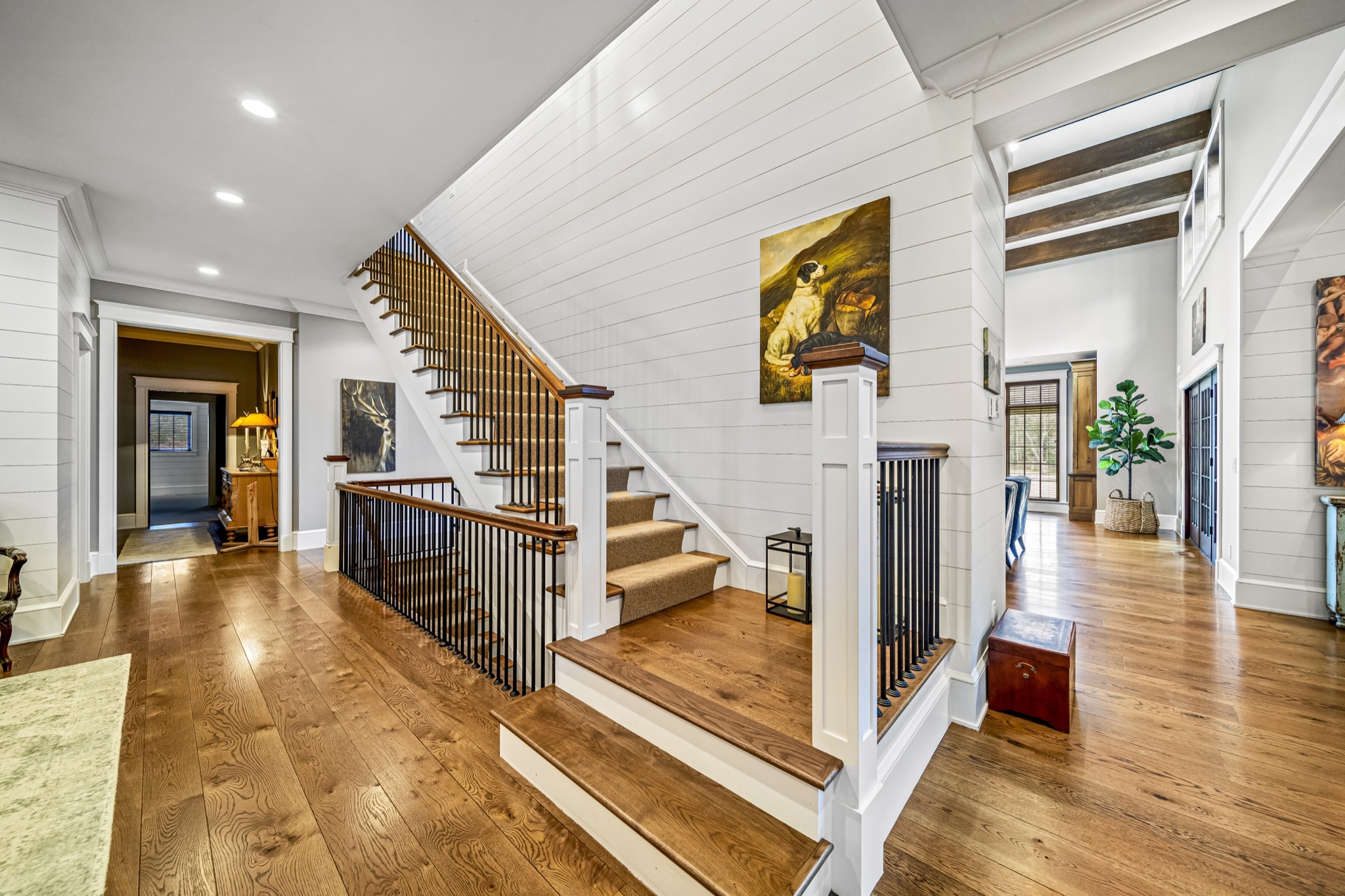 Grand staircase with iron balusters, reclaimed wood railing, shiplap walls, and oil painting beneath exposed timber beams — luxury custom home by Skoda Construction, Northeast Ohio
