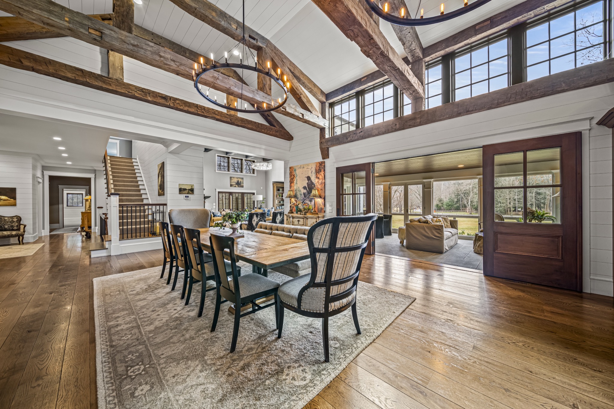 Formal dining area beneath soaring timber-frame ceiling with iron chandelier, shiplap walls, and French doors — custom home by Skoda Construction, Northeast Ohio