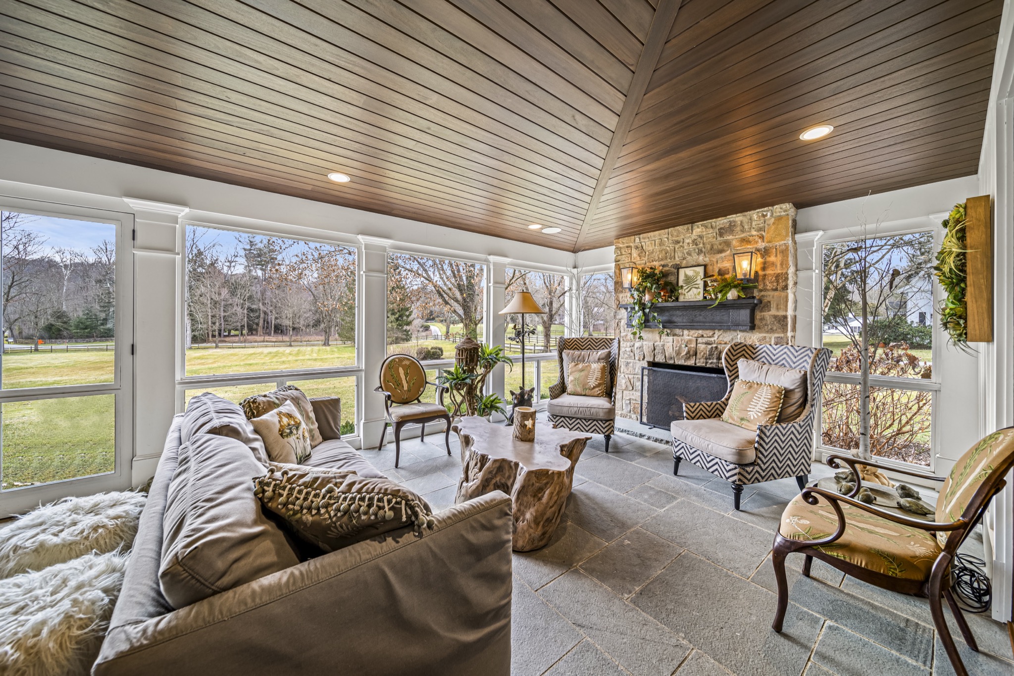 Four-season sunroom with tongue-and-groove wood ceiling, natural stone fireplace, bluestone floor, and panoramic windows — luxury home by Skoda Construction, Northeast Ohio