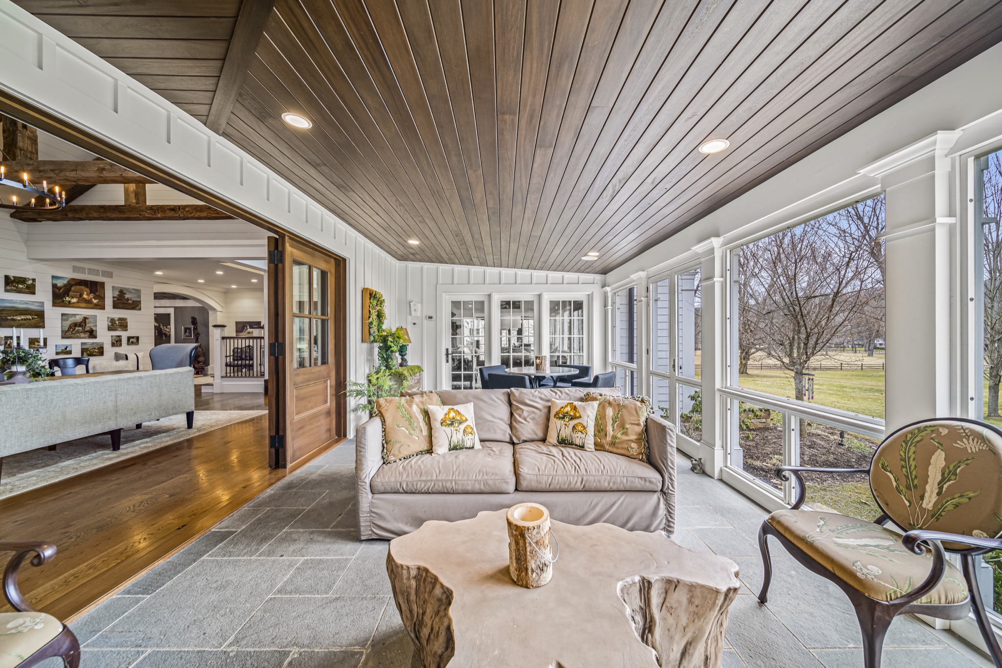 Screened porch with stained wood plank ceiling, bluestone floor, live-edge coffee table, and panoramic views of manicured grounds — luxury outdoor living by Skoda Construction, Northeast Ohio