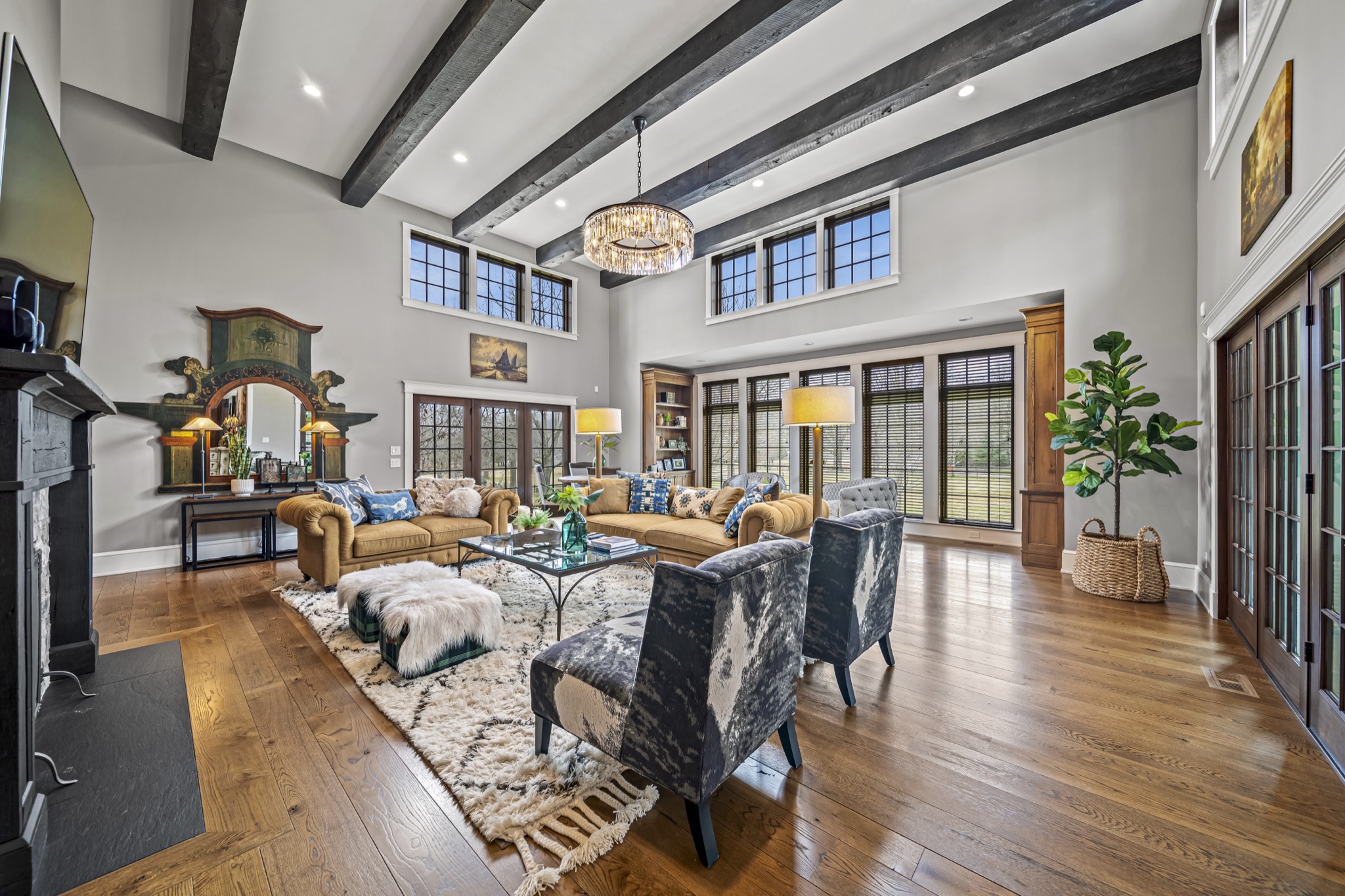 Vaulted family room with exposed dark timber beams, crystal chandelier, tufted furnishings, and wall of French doors — luxury custom home by Skoda Construction, Northeast Ohio