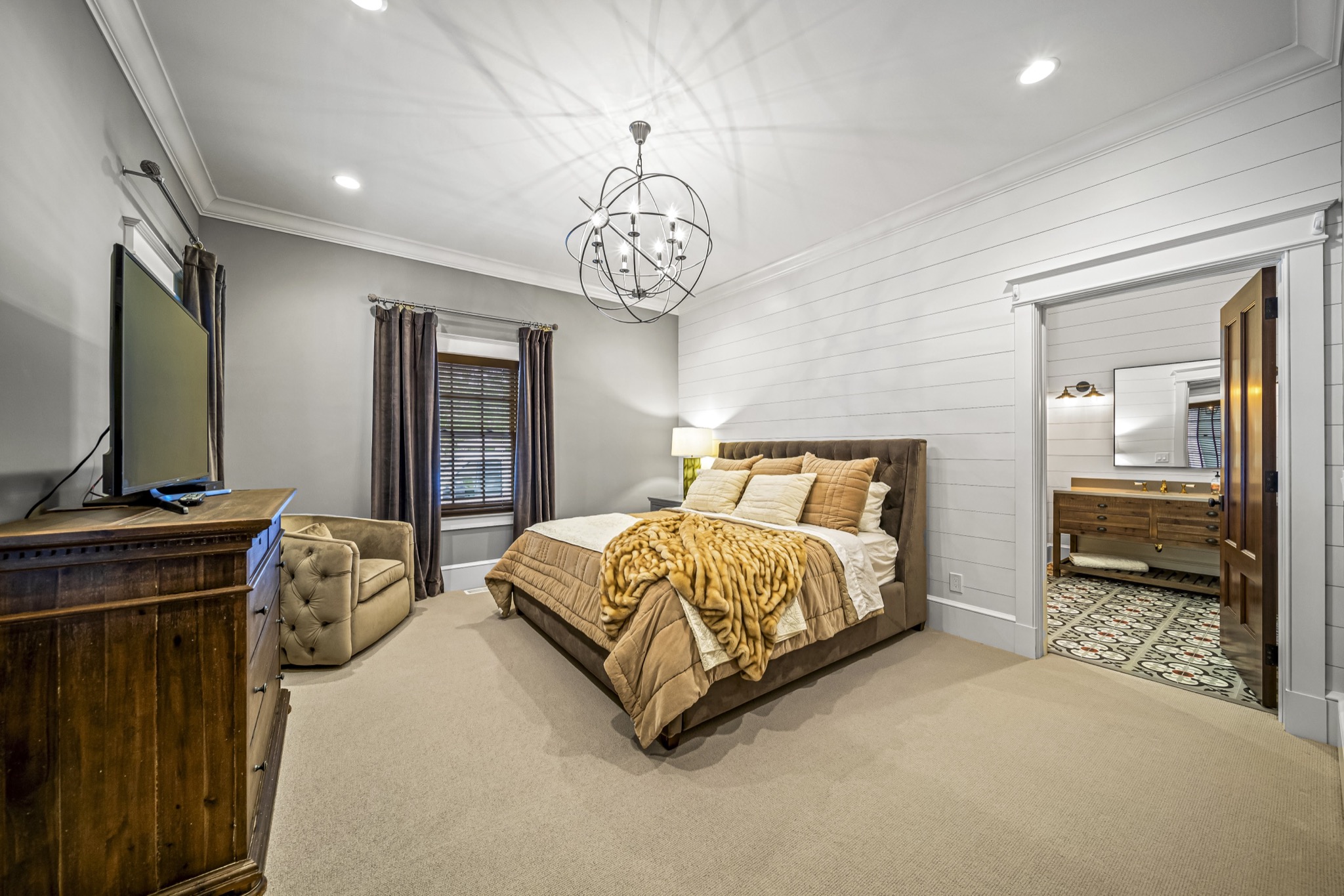 Guest bedroom with iron orb chandelier, shiplap ceiling, reclaimed wood furniture, and doorway to patterned tile bathroom — luxury custom home by Skoda Construction, Northeast Ohio