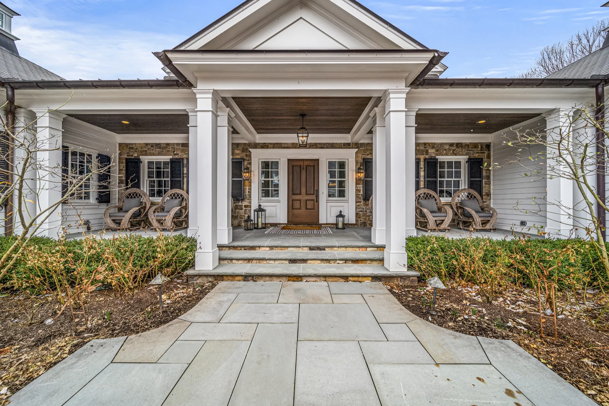 Covered front portico with stone-veneer columns, bluestone walkway, and Adirondack seating — luxury custom farmhouse by Skoda Construction, Northeast Ohio