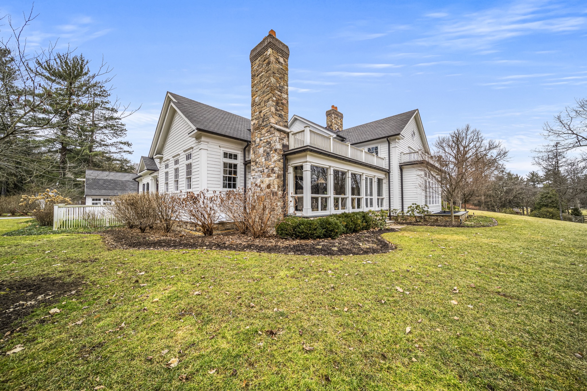 Rear elevation showcasing stone chimney, sunroom wall of windows, and second-floor balcony — luxury custom home by Skoda Construction, Northeast Ohio