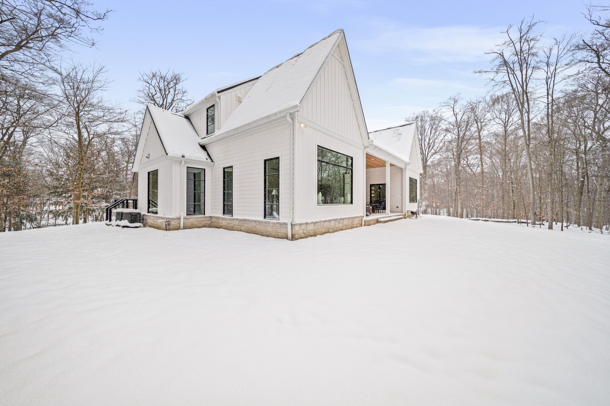 Rear elevation of modern estate with dramatic peaked gable, floor-to-ceiling glass wall, and stone base surrounded by snowy woodland — custom home by Skoda Construction, Northeast Ohio