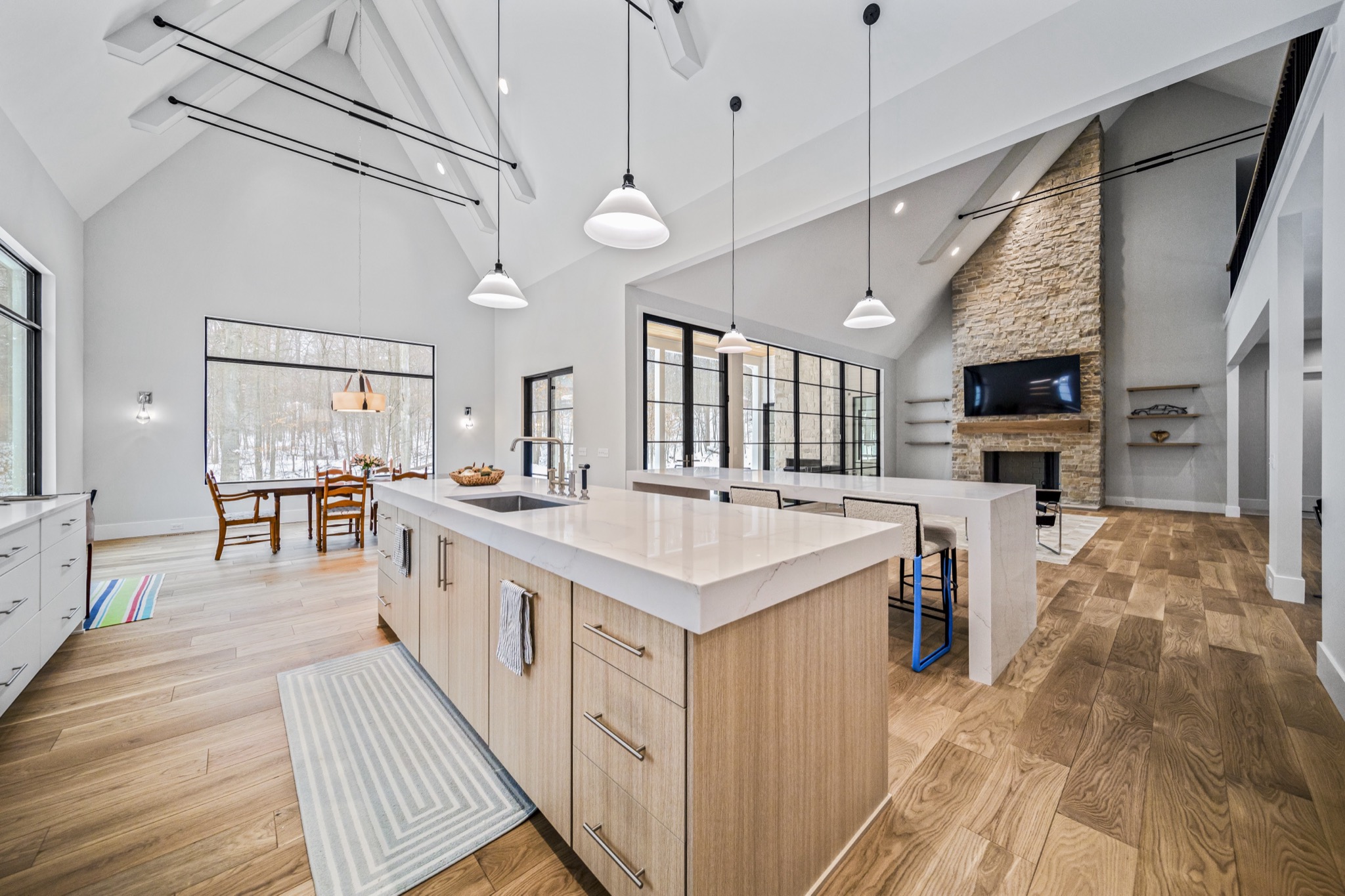 Open-concept luxury kitchen with dual islands, waterfall quartz countertops, pendant lighting, and soaring cathedral ceiling with exposed beams — custom home by Skoda Construction, Northeast Ohio