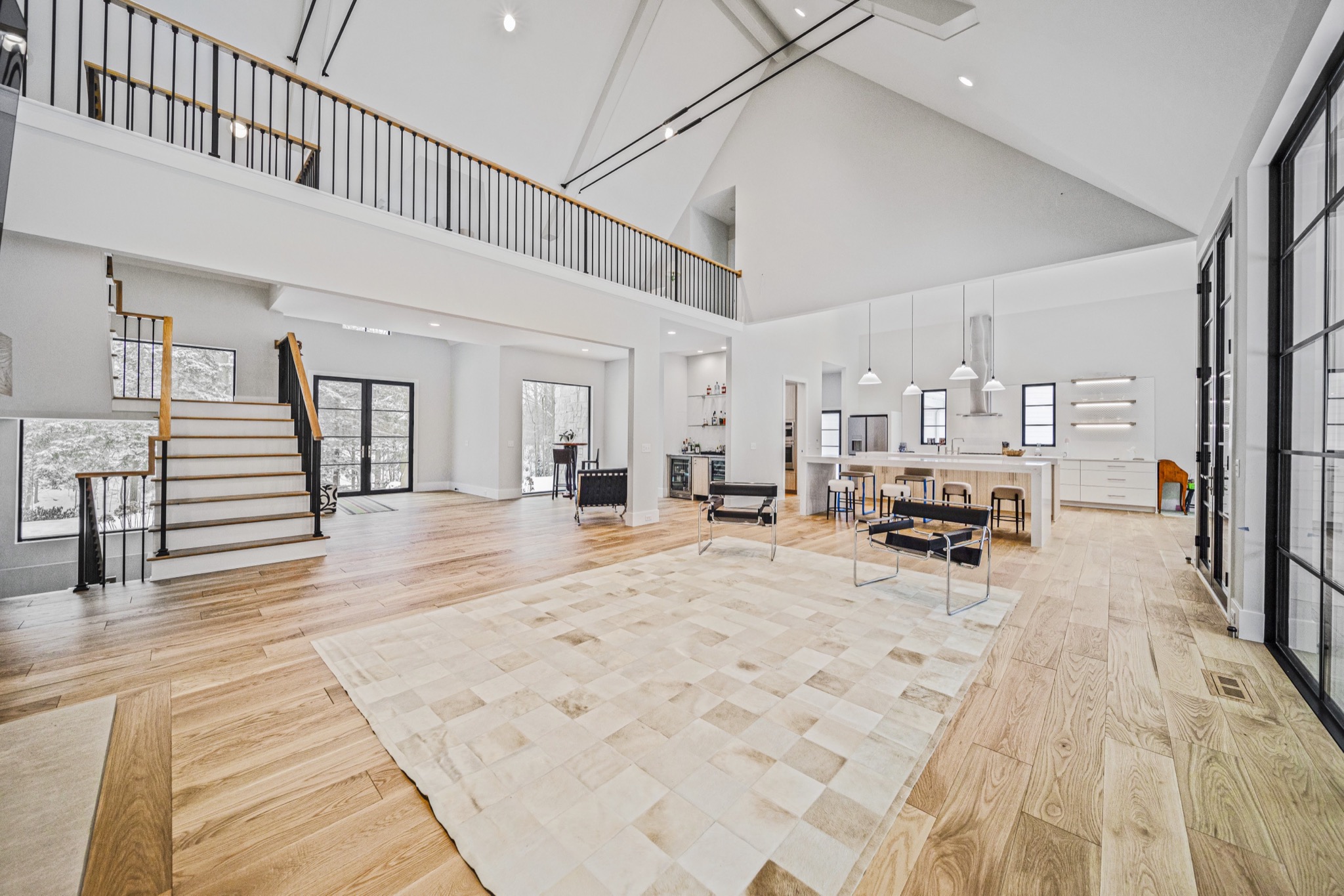 Two-story great room with dramatic cathedral ceiling, modern open staircase, and expansive glass walls flooding the space with natural light — Skoda Construction custom home